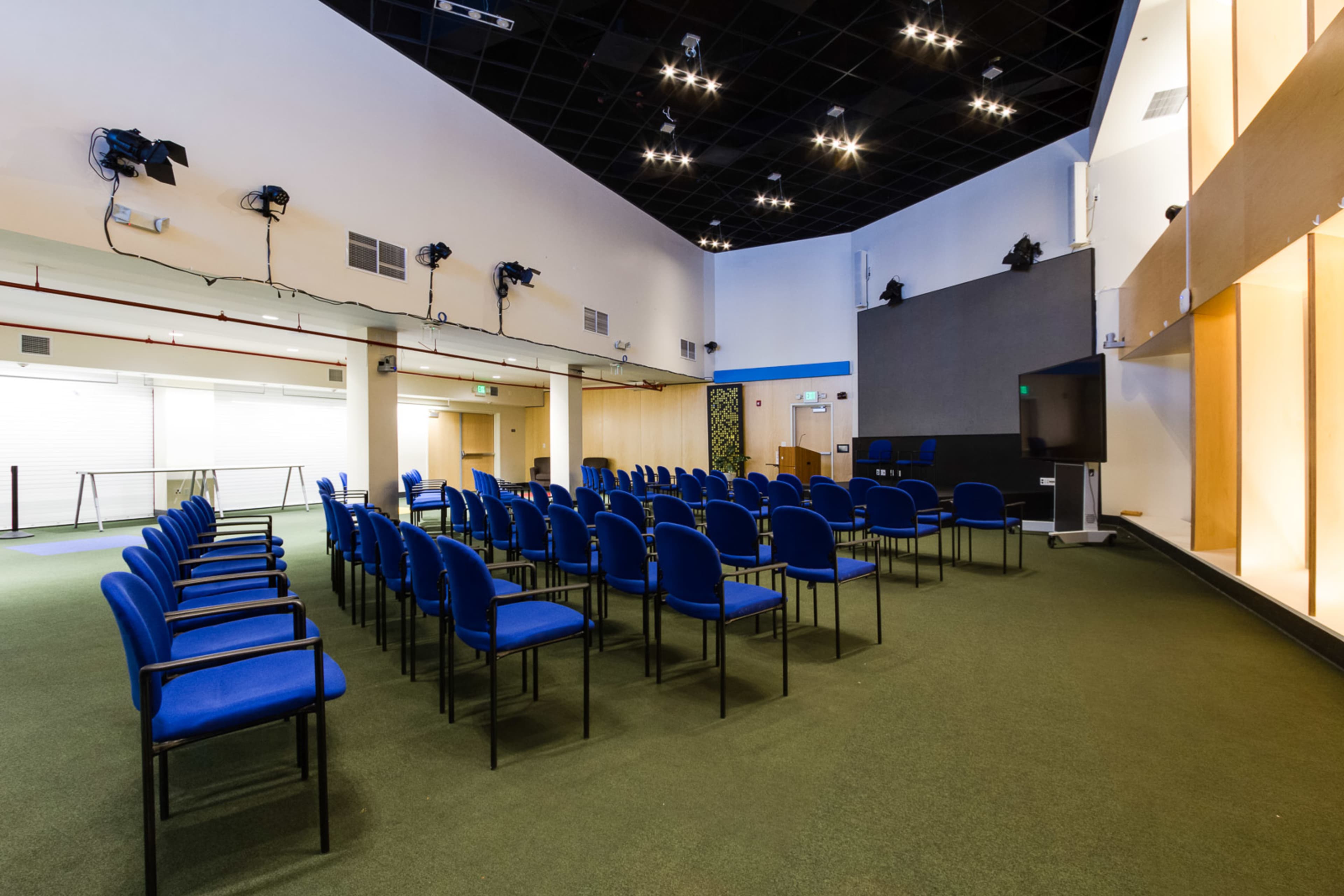A conference room set up with blue chairs arranged in rows facing a large screen and a presentation area.