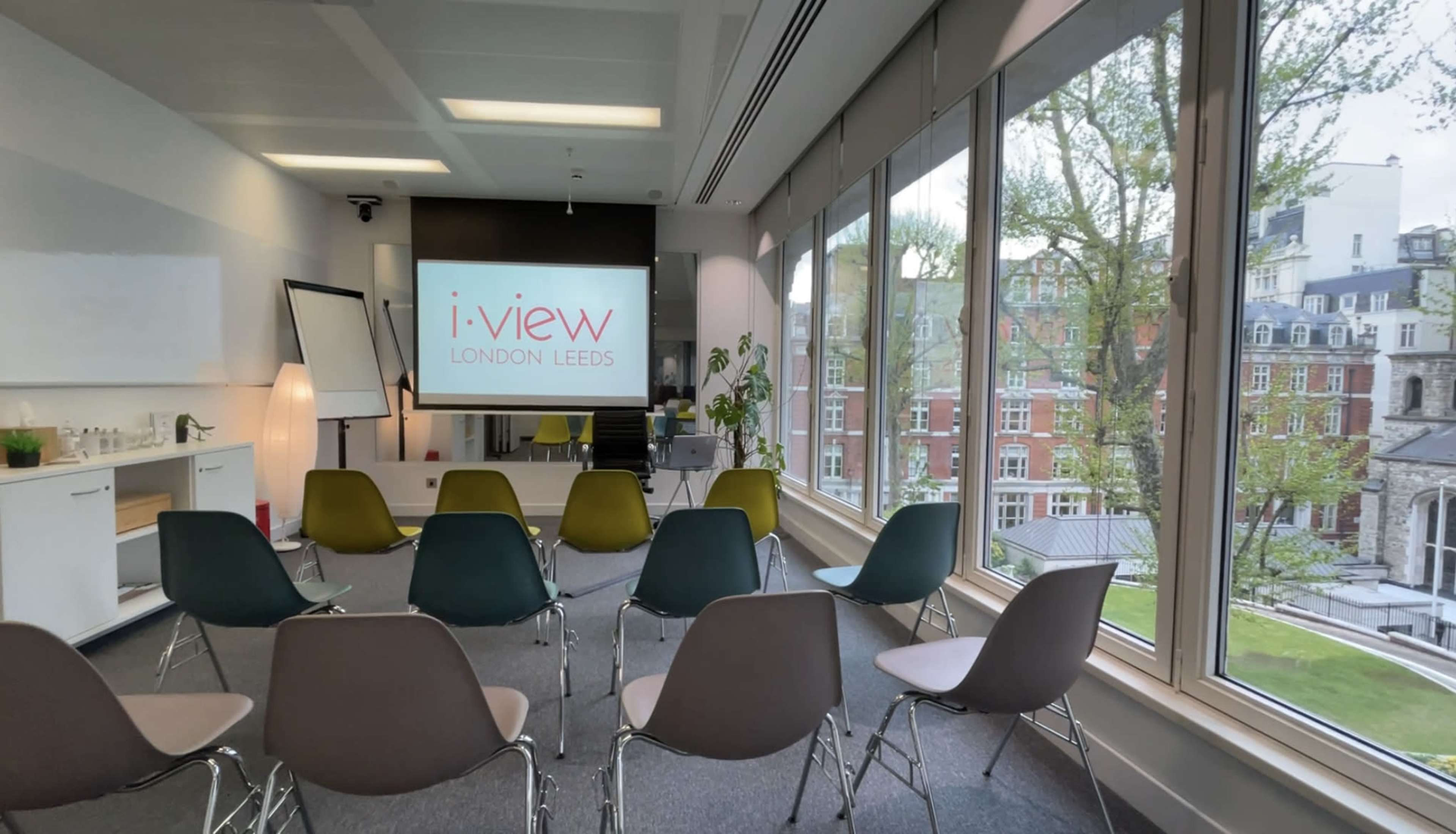 A conference room features a projector screen displaying the text "i-view LONDON LEEDS" and is arranged with several chairs facing it.