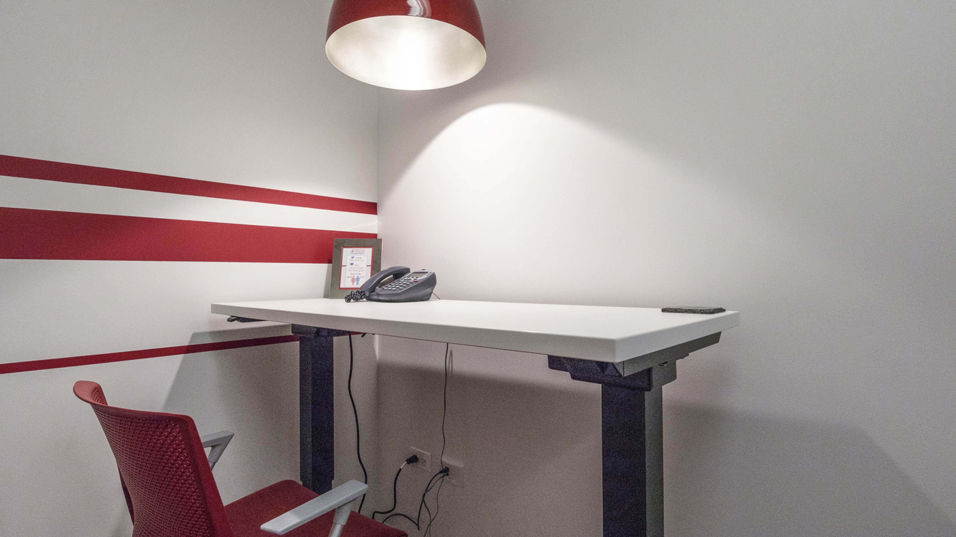 A minimalist office space features a white desk with a telephone, a chair, and red wall stripes.