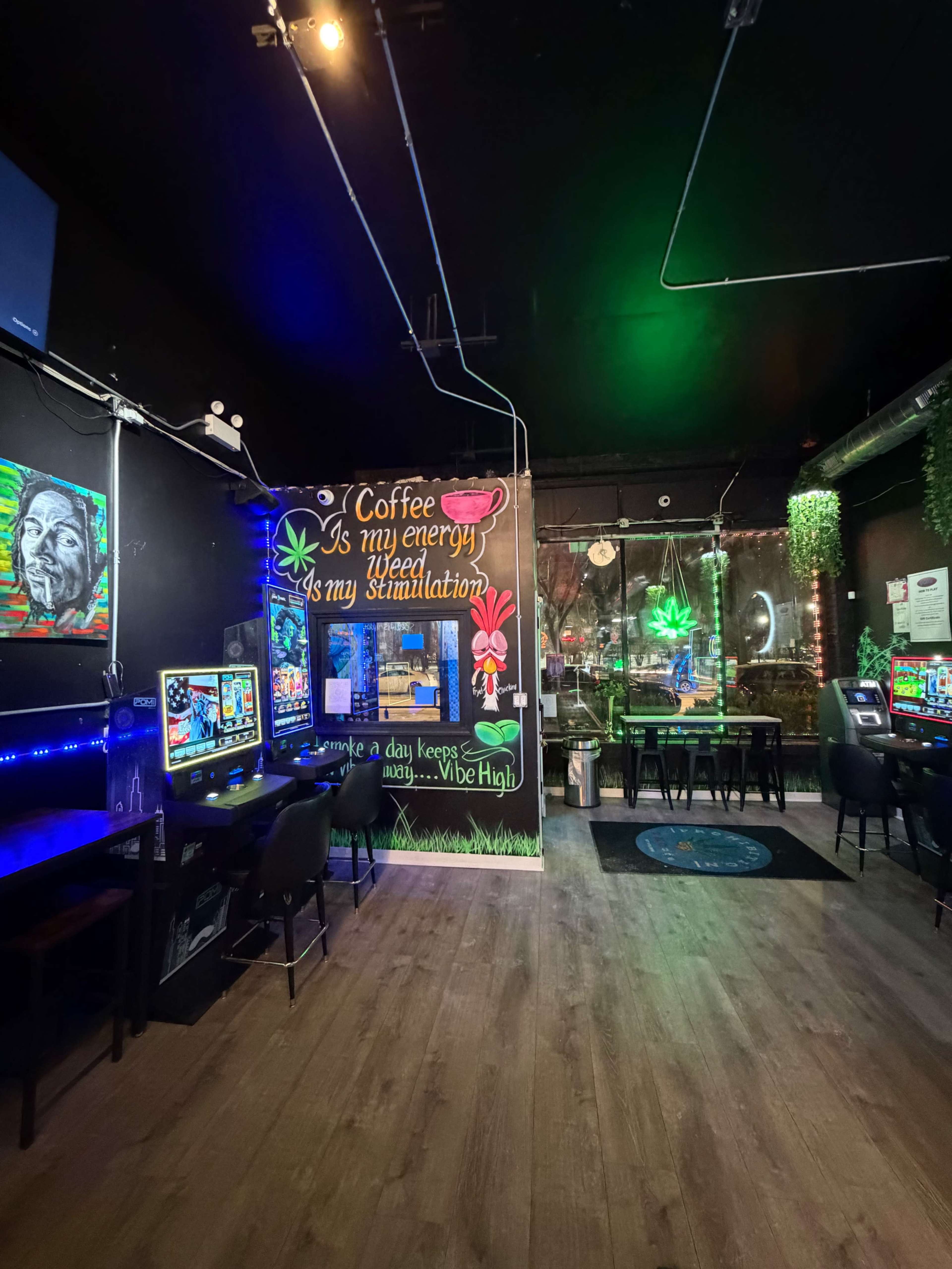 The image shows a modern gaming lounge with colorful wall art, gaming machines, and seating areas illuminated by ambient lighting.