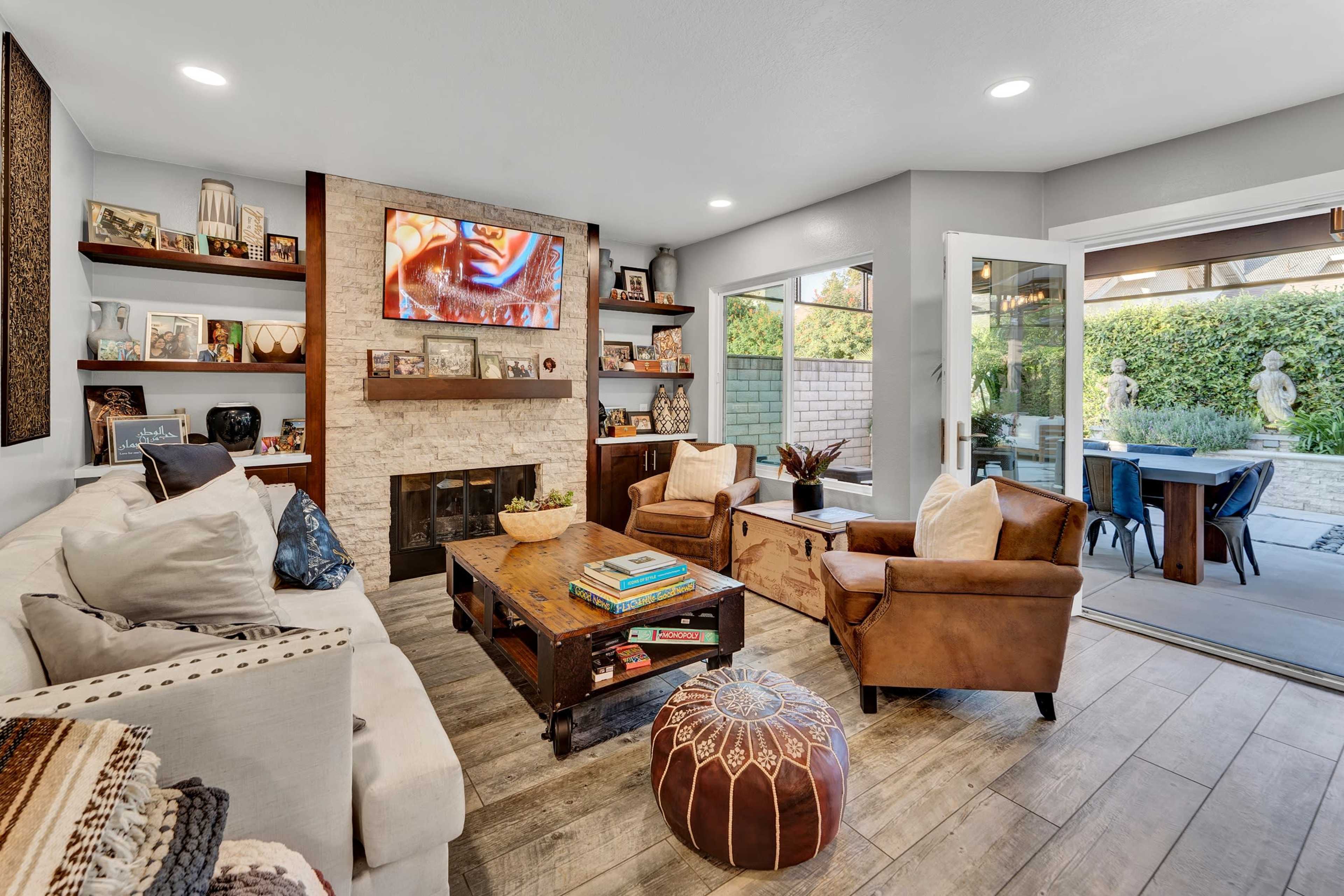 The living room features a beige sofa, a wooden coffee table stacked with books, and leather armchairs, with an entertainment center displaying a TV and decorative items.