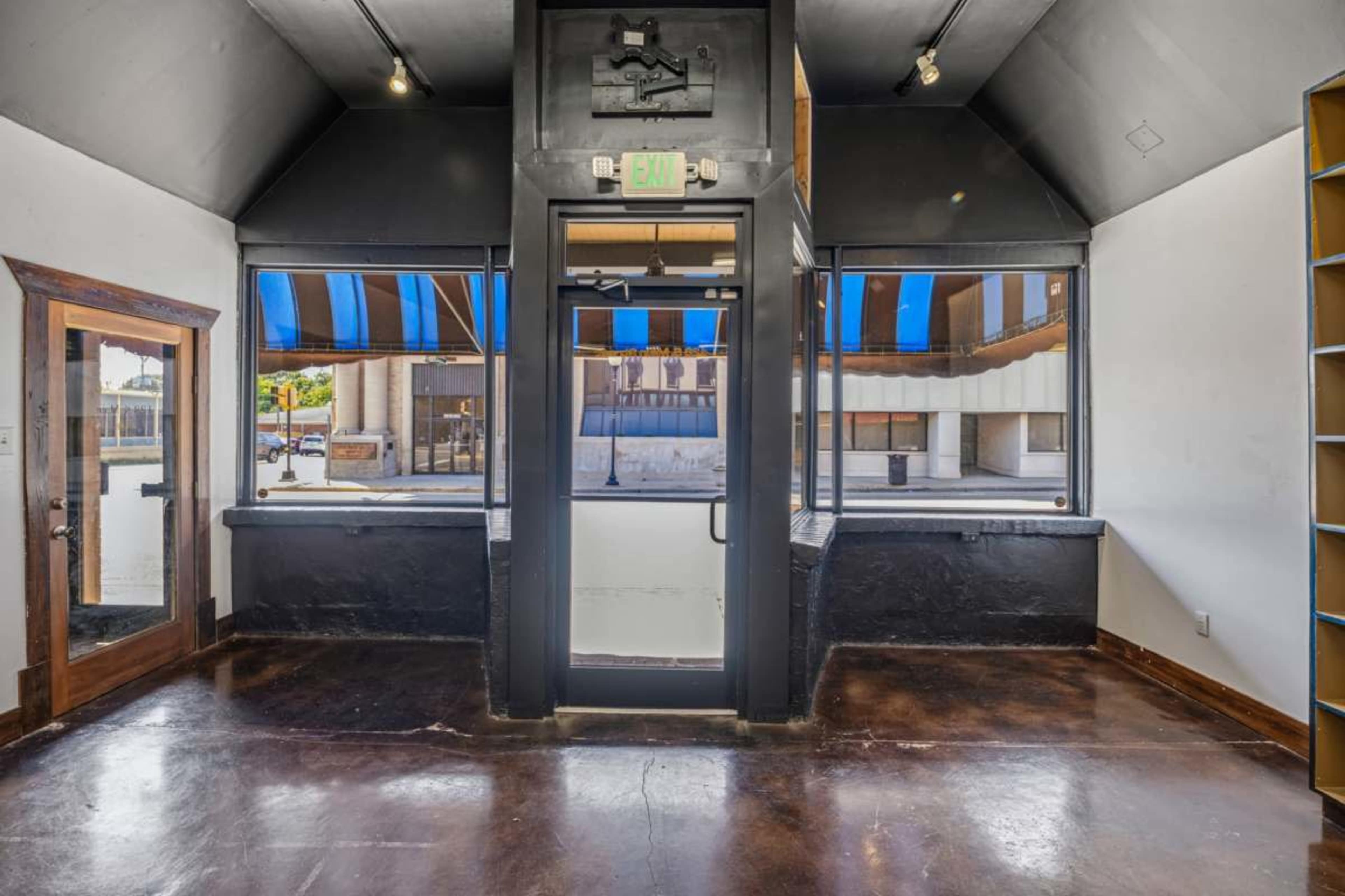 The image shows a corner space with large windows, a door at the center, and shelves on one side of the wall.