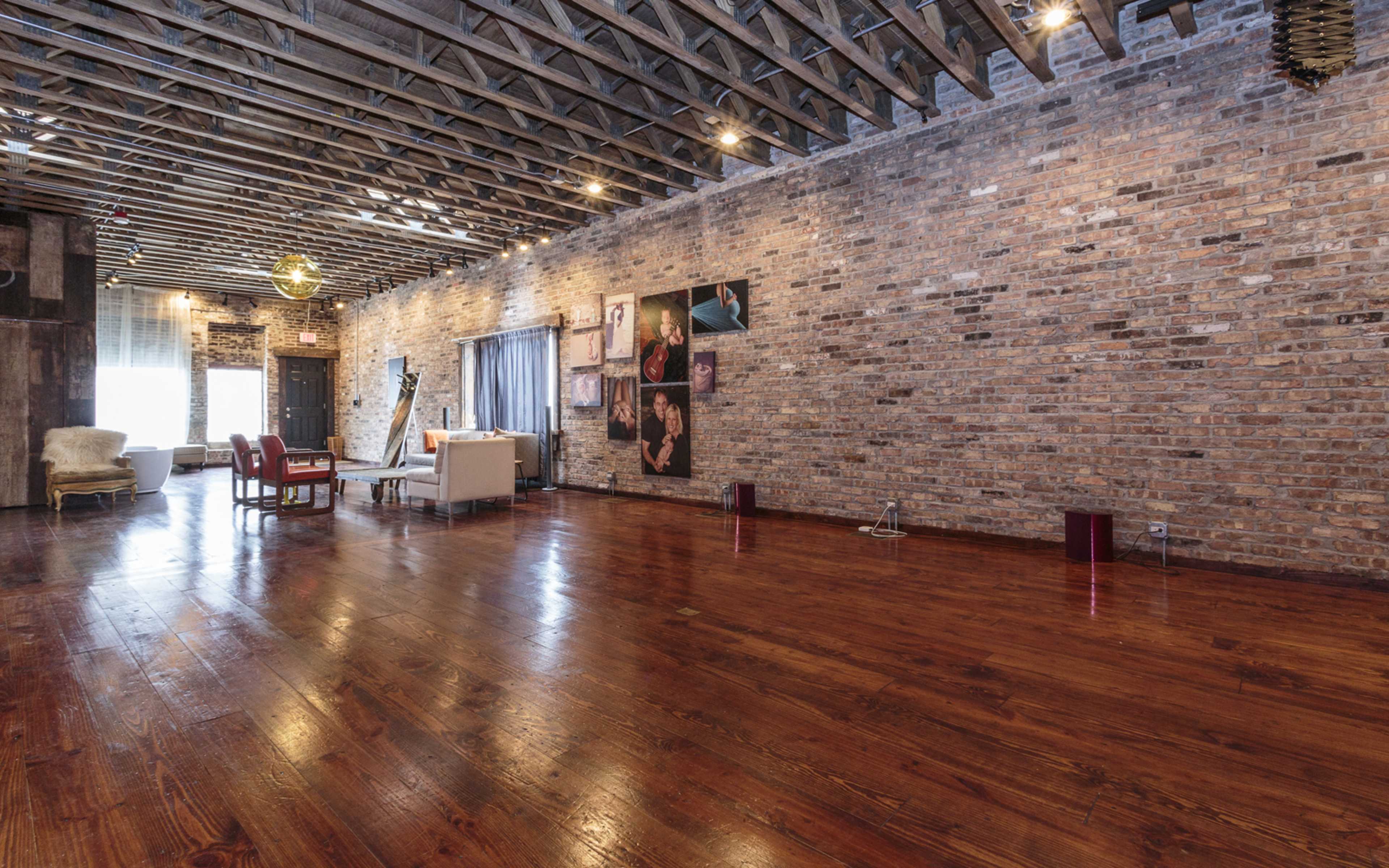 A spacious room with exposed brick walls, wooden flooring, and a mix of modern and vintage furniture.