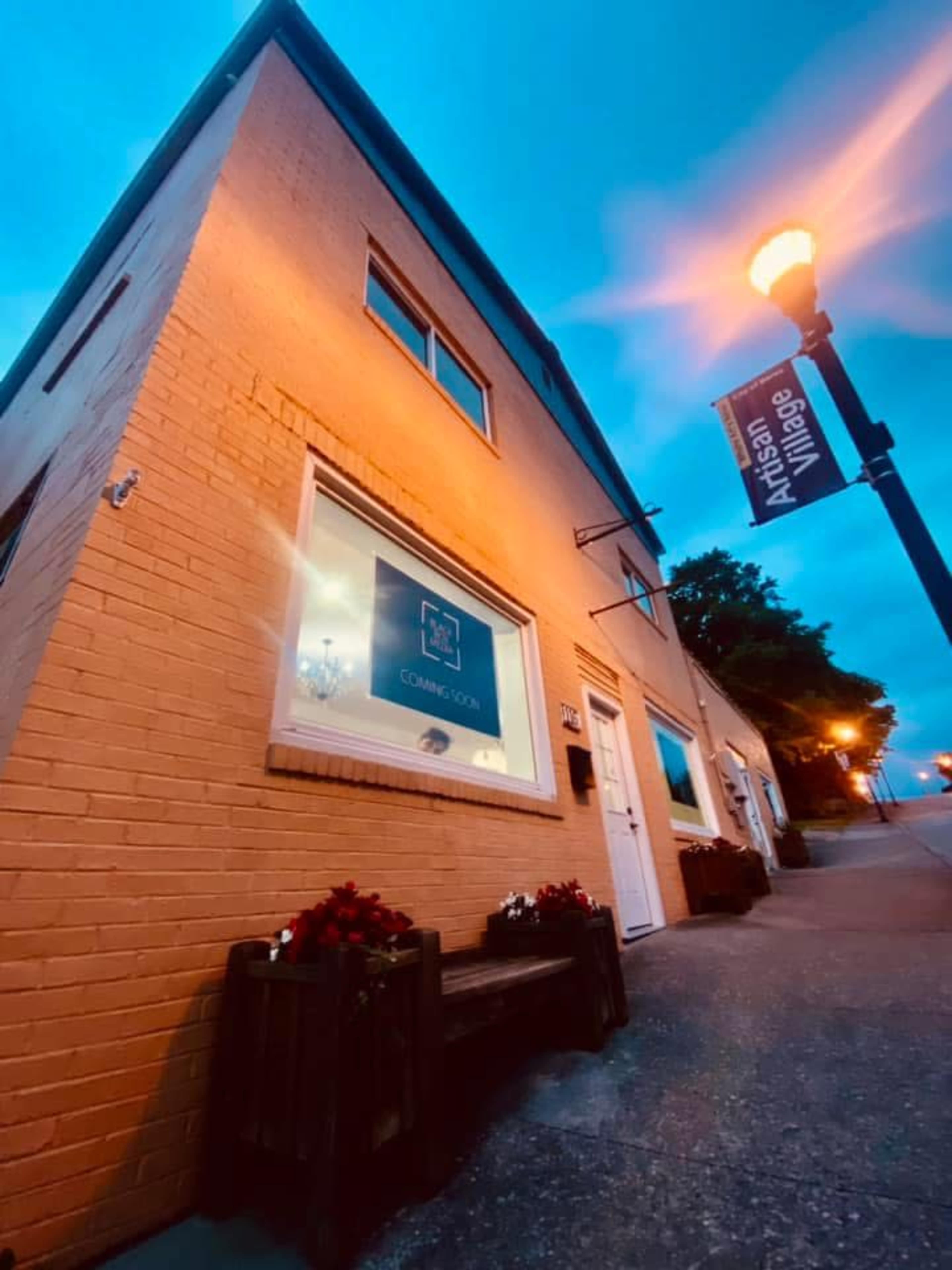 The image shows a building with a sign reading "Artisan Village" and a lit streetlamp nearby, set against a twilight sky.