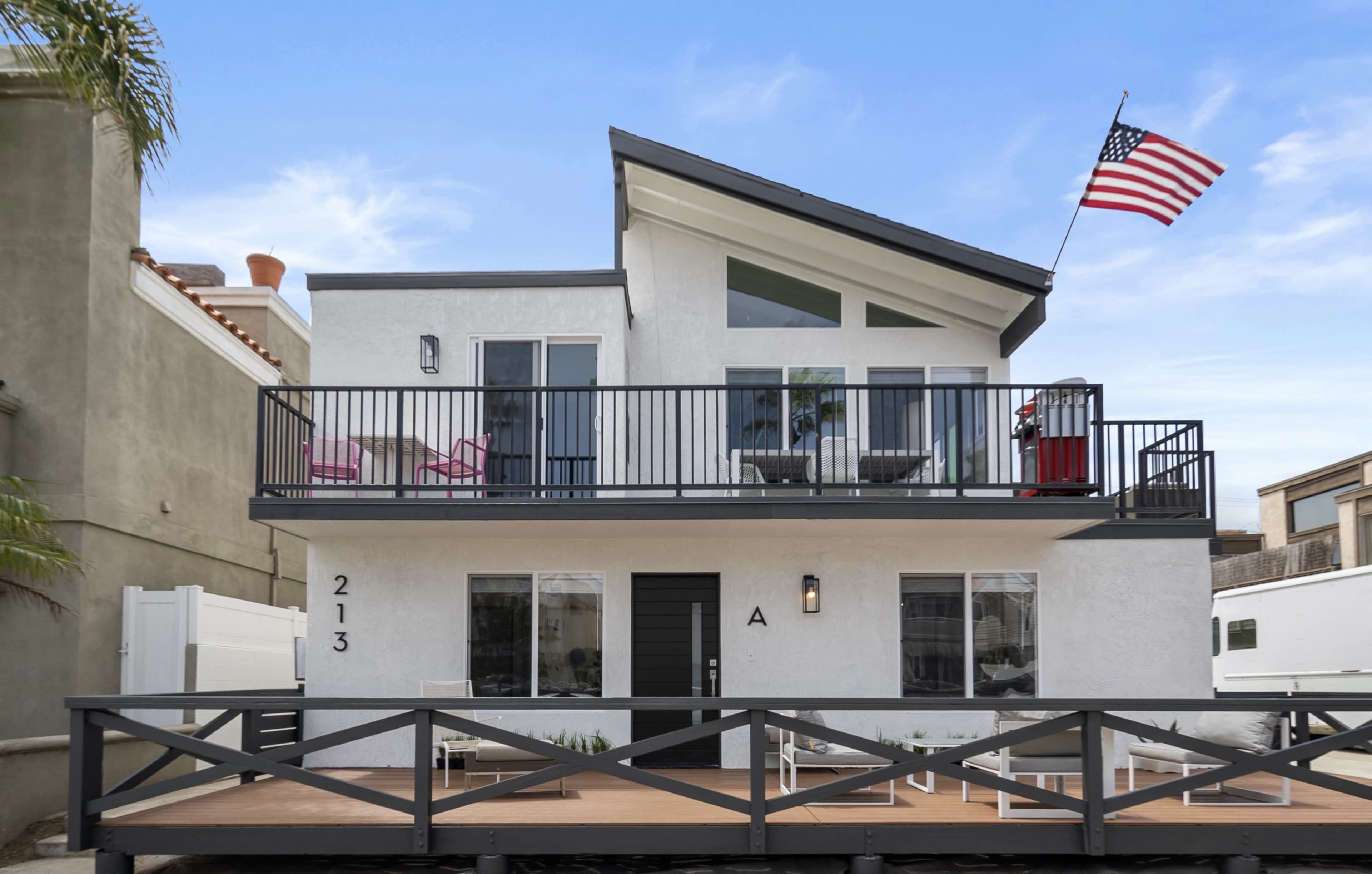 A modern two-story white house with a sloping roof, a balcony, and an American flag flying in front.