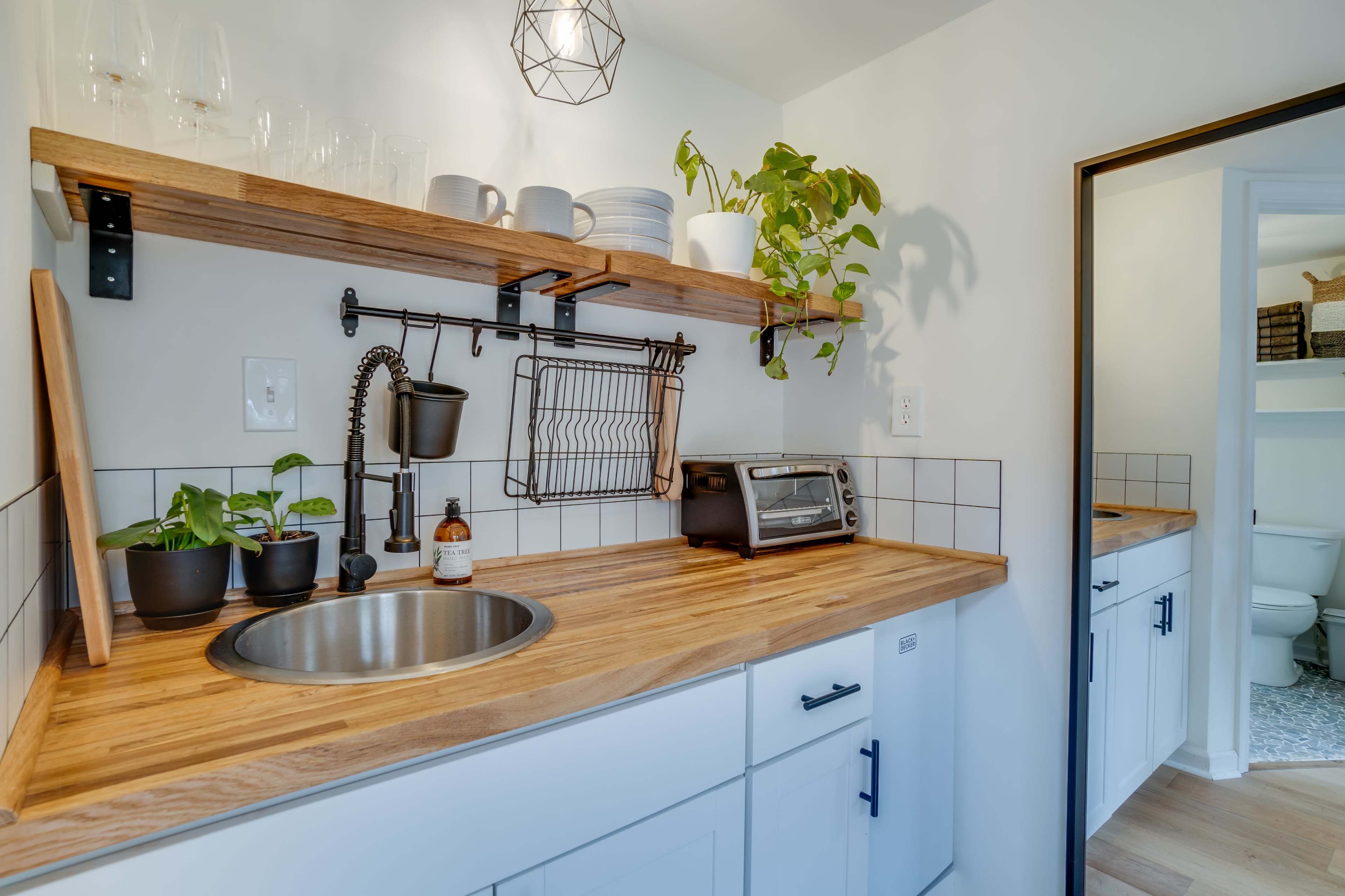 A compact kitchen area featuring wooden shelves, a stainless steel sink, a countertop toaster, and plants on display.