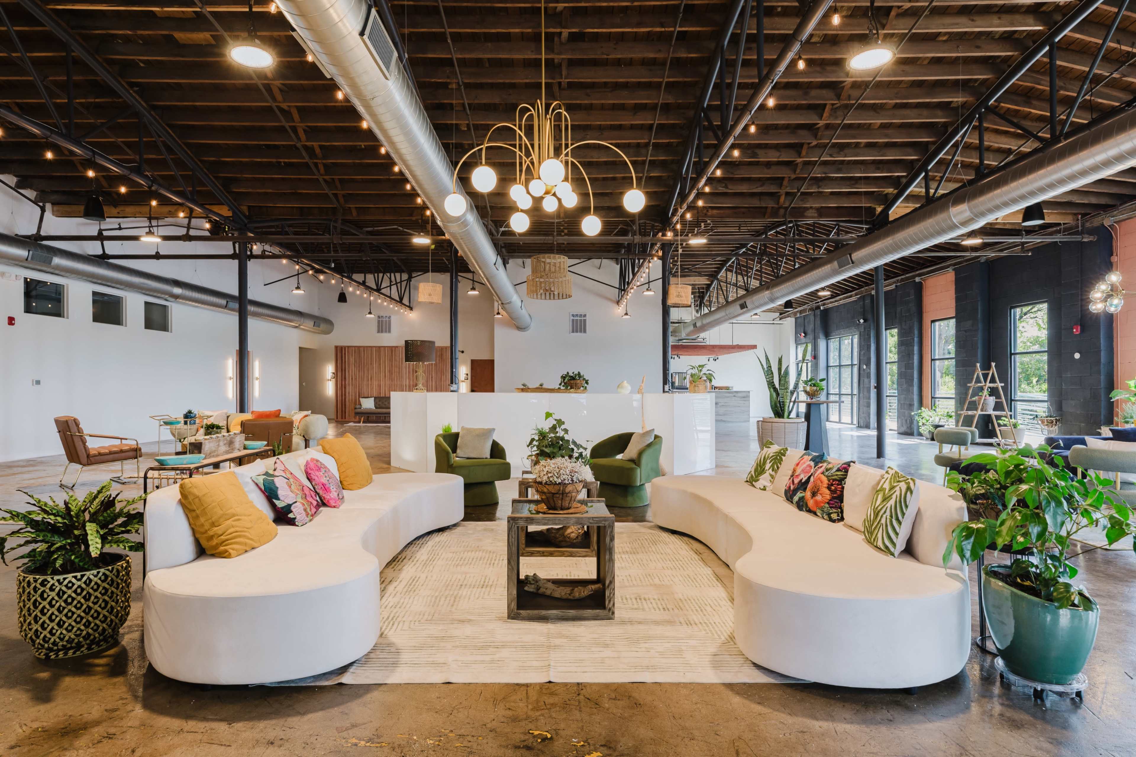 The image depicts a spacious, modern lounge area with curved seating, decorative plants, and ambient lighting.