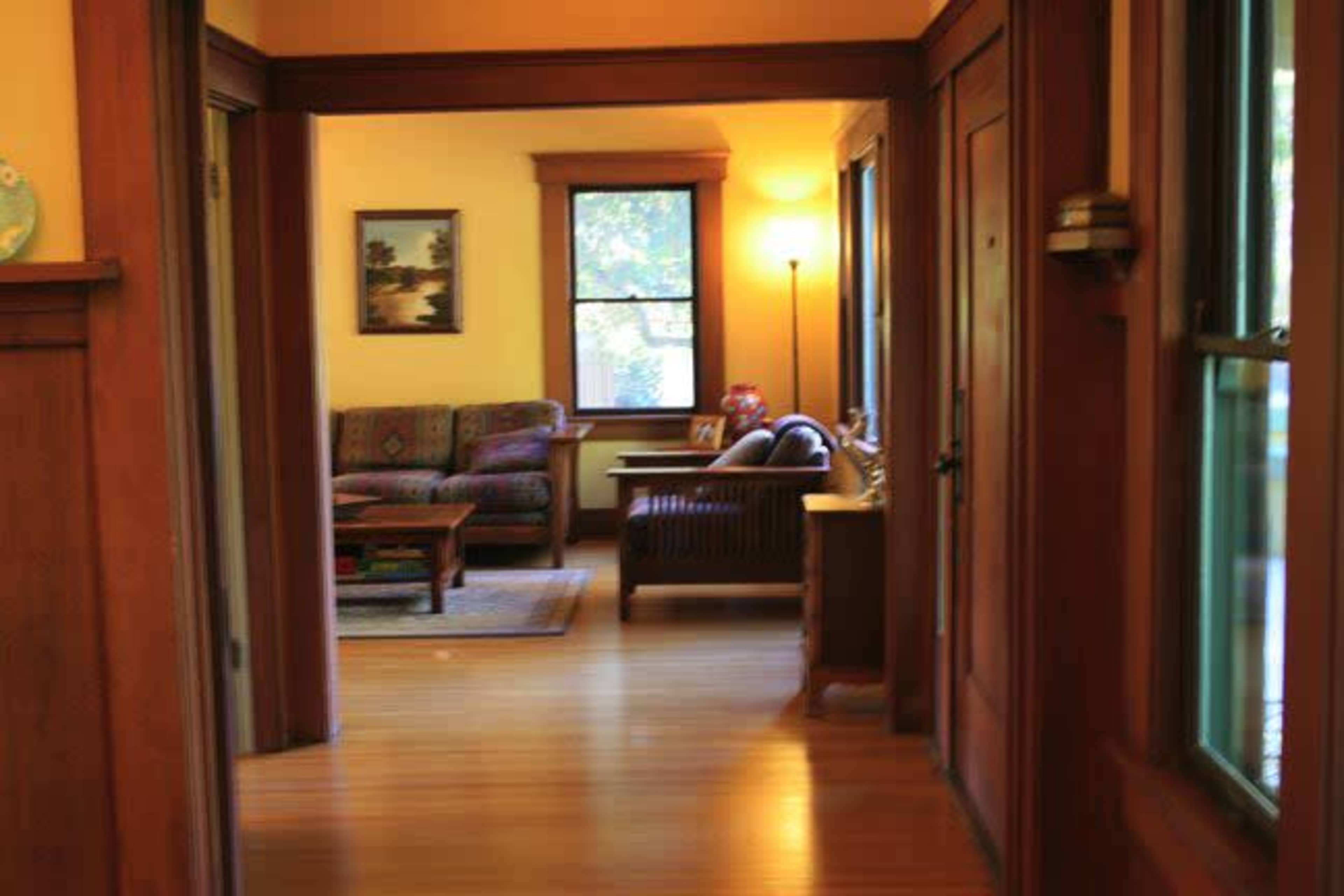 A hallway leading to a living room with a sofa, coffee table, and windows allowing natural light.