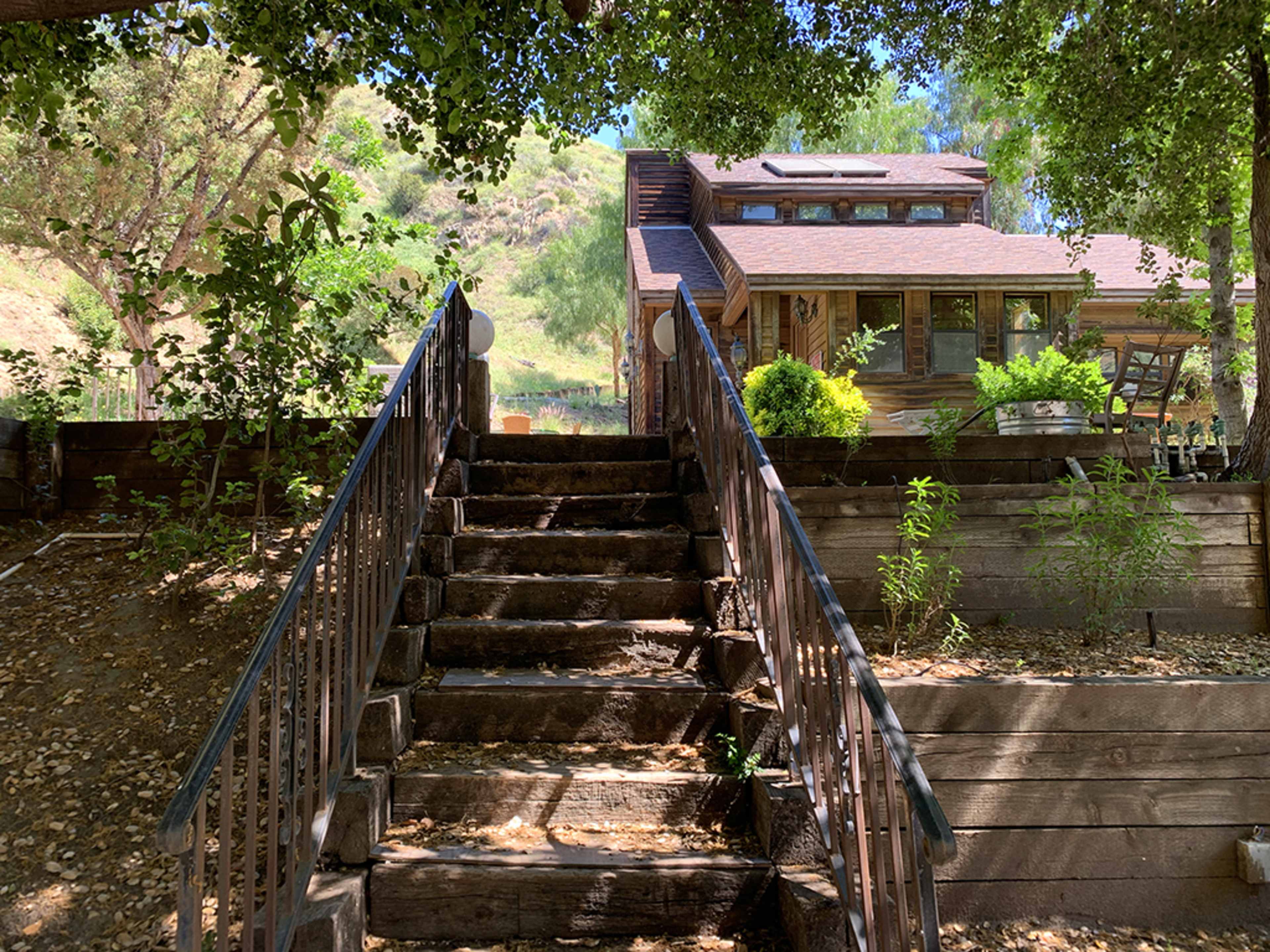 A set of wooden stairs leads up to a house surrounded by trees and greenery.