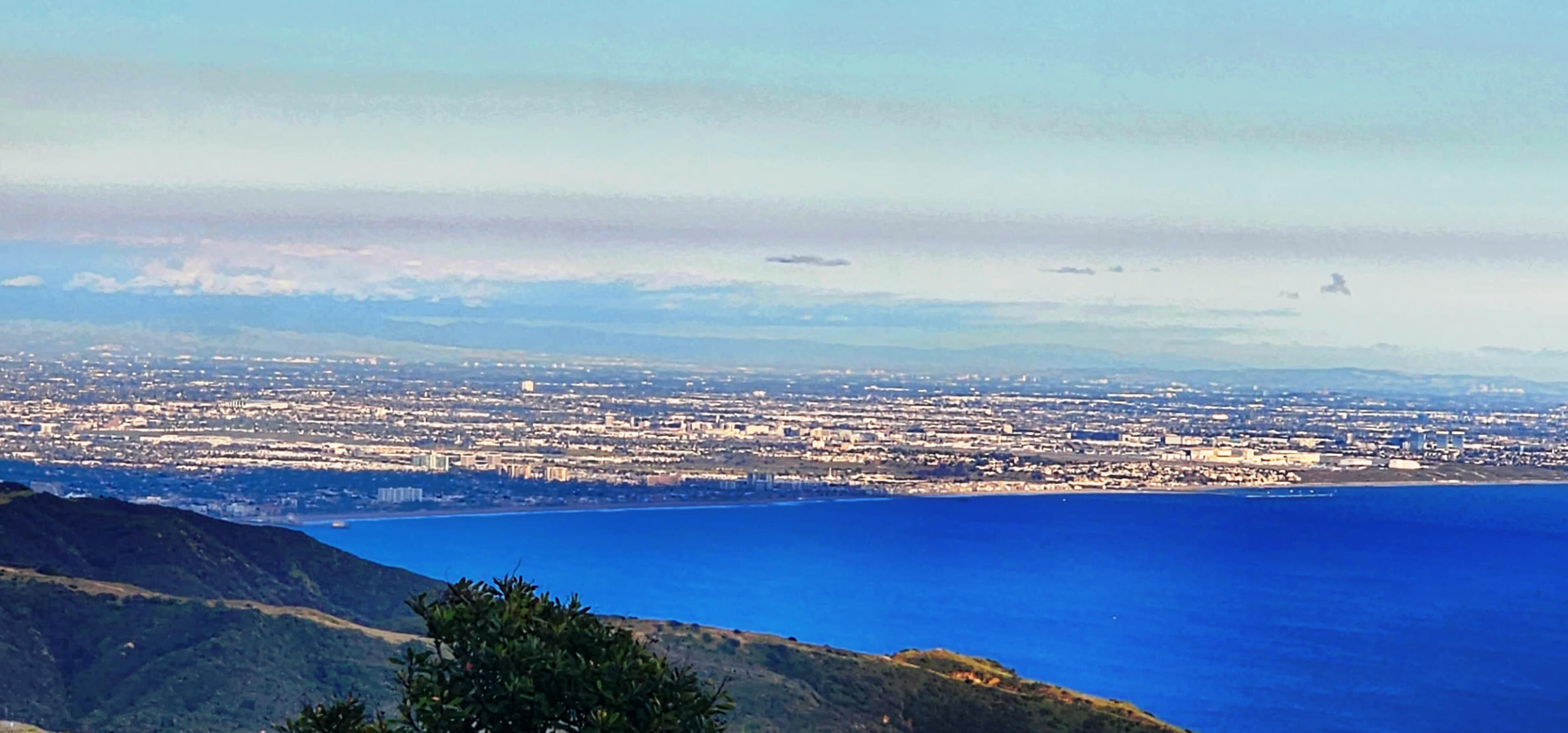 The image shows a coastal view with a large body of water extending to the horizon and a cityscape visible in the distance against a clear sky.