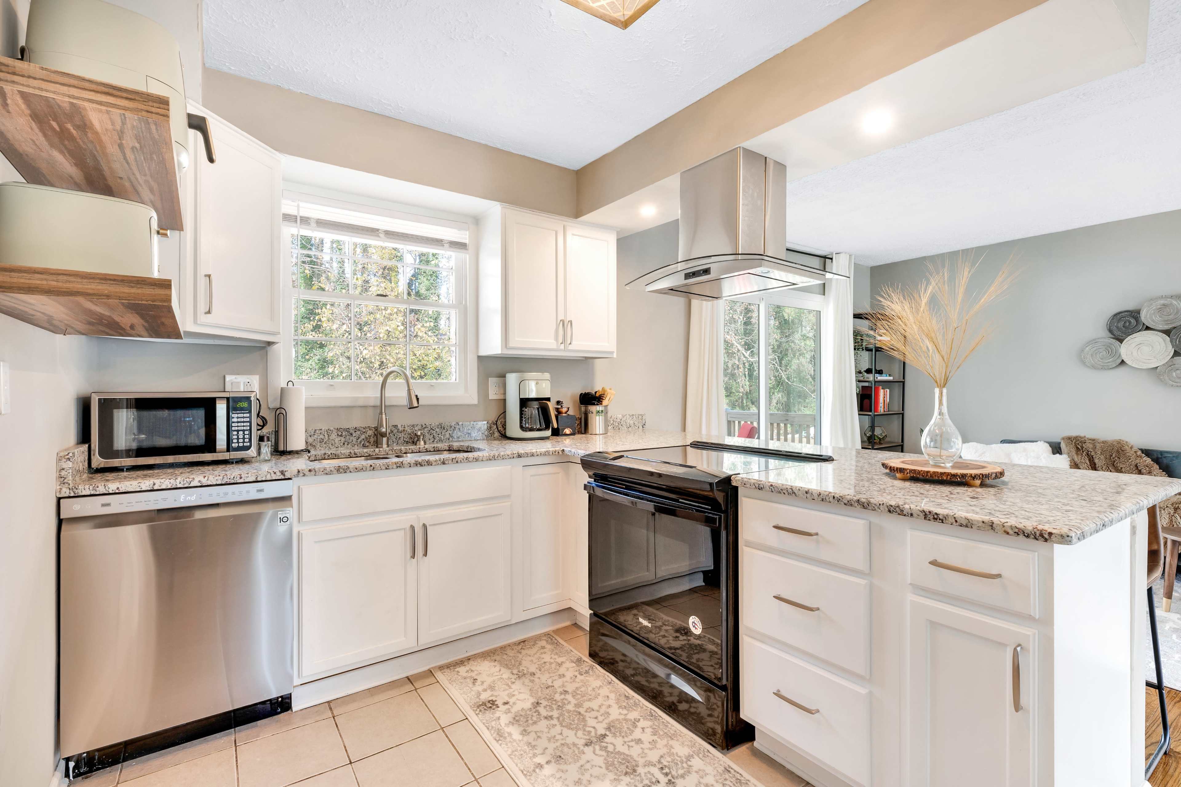 A modern kitchen with white cabinets, stainless steel appliances, and a window overlooking a garden area.