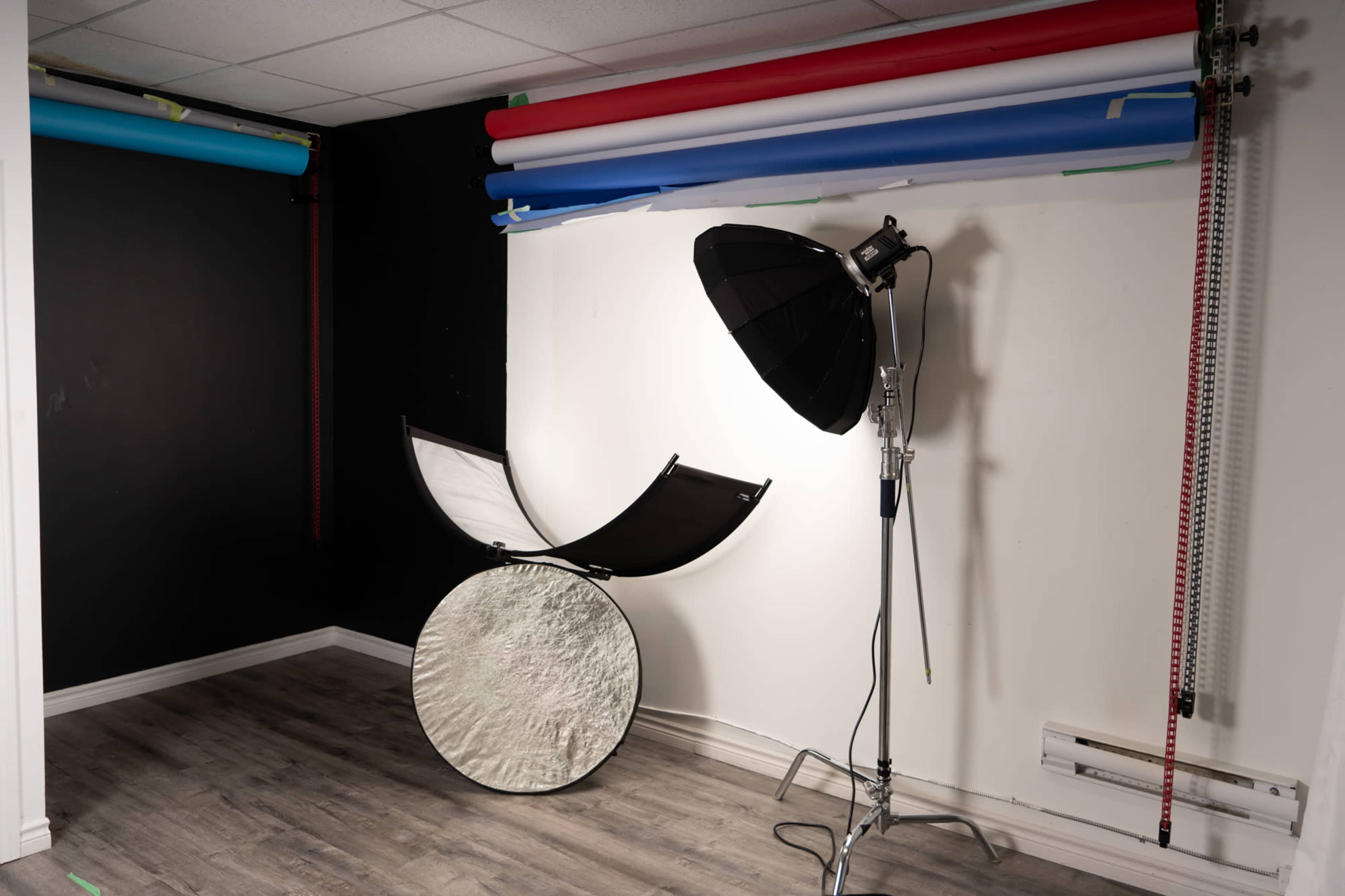 A photography studio setup with backdrop rolls mounted on the wall and lighting equipment positioned beside a reflector.