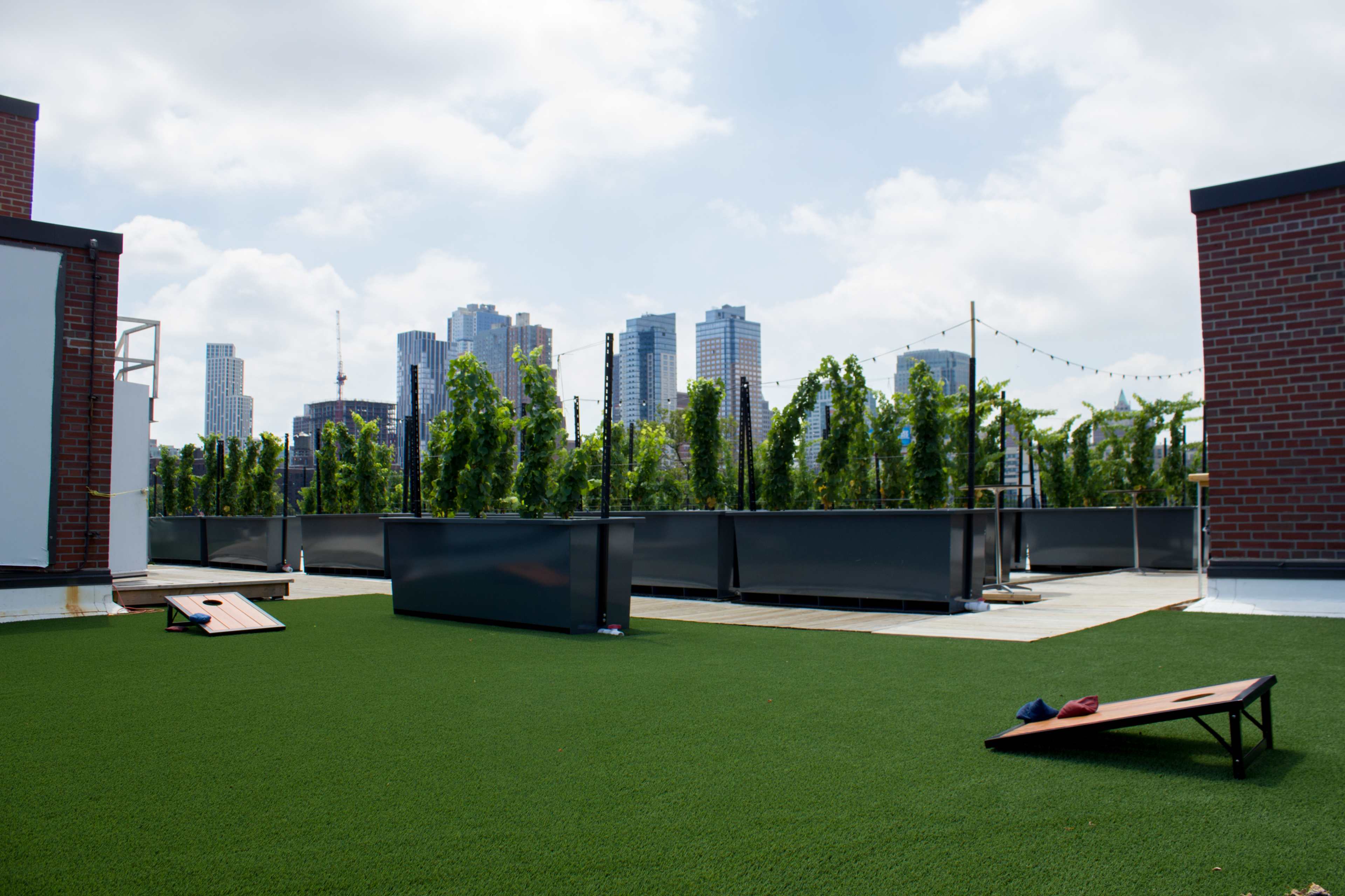 A rooftop area features green turf, outdoor benches, and a skyline of tall buildings in the background.