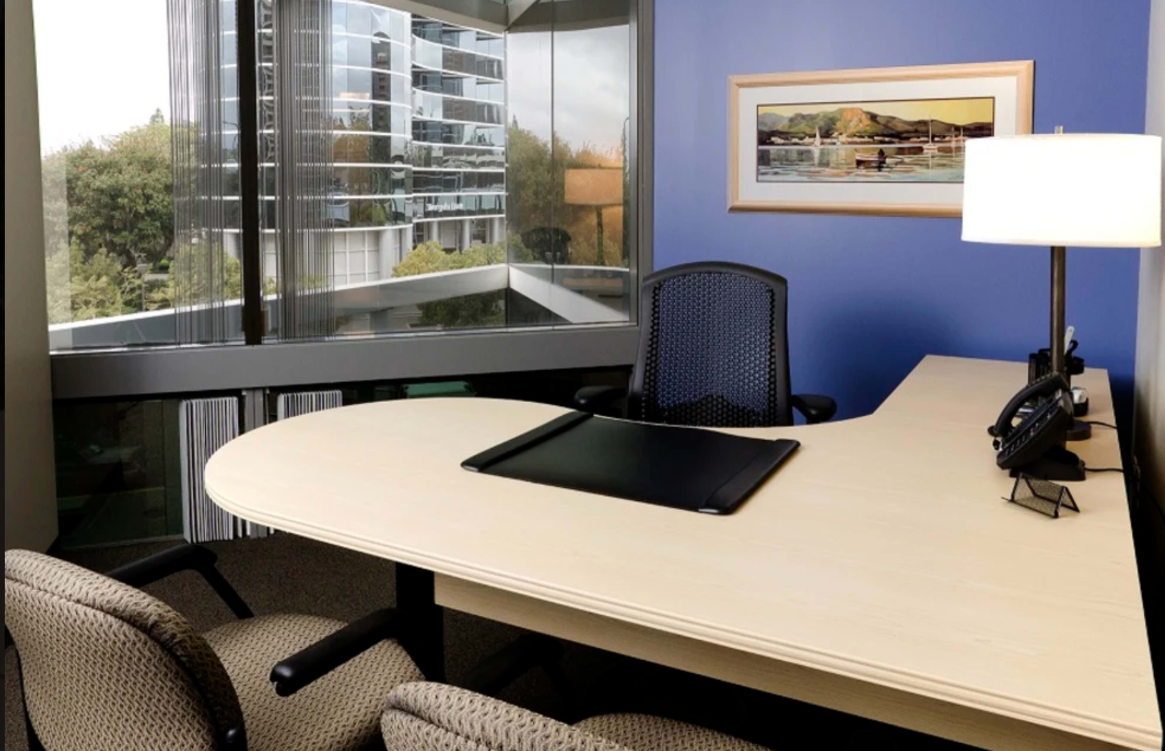 A modern office features a large desk, two chairs, and a window overlooking a cityscape.