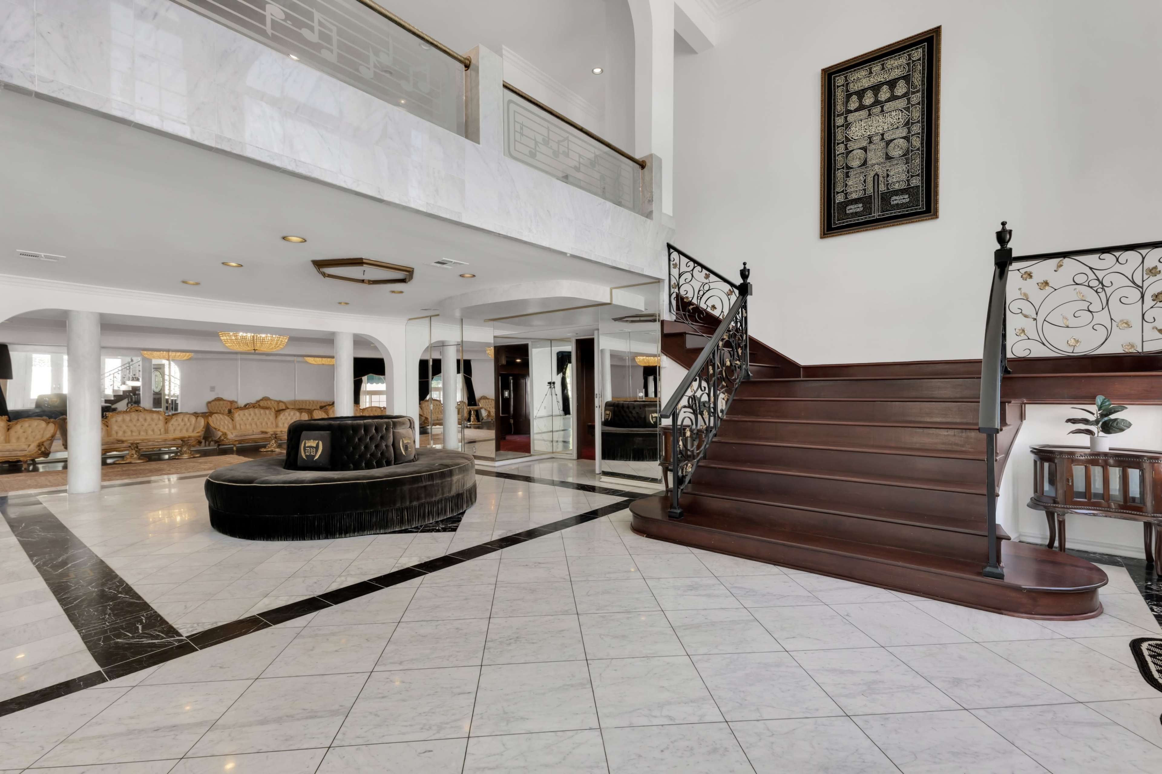 The image shows a spacious foyer with a grand staircase, marble flooring, and a curved seating area.