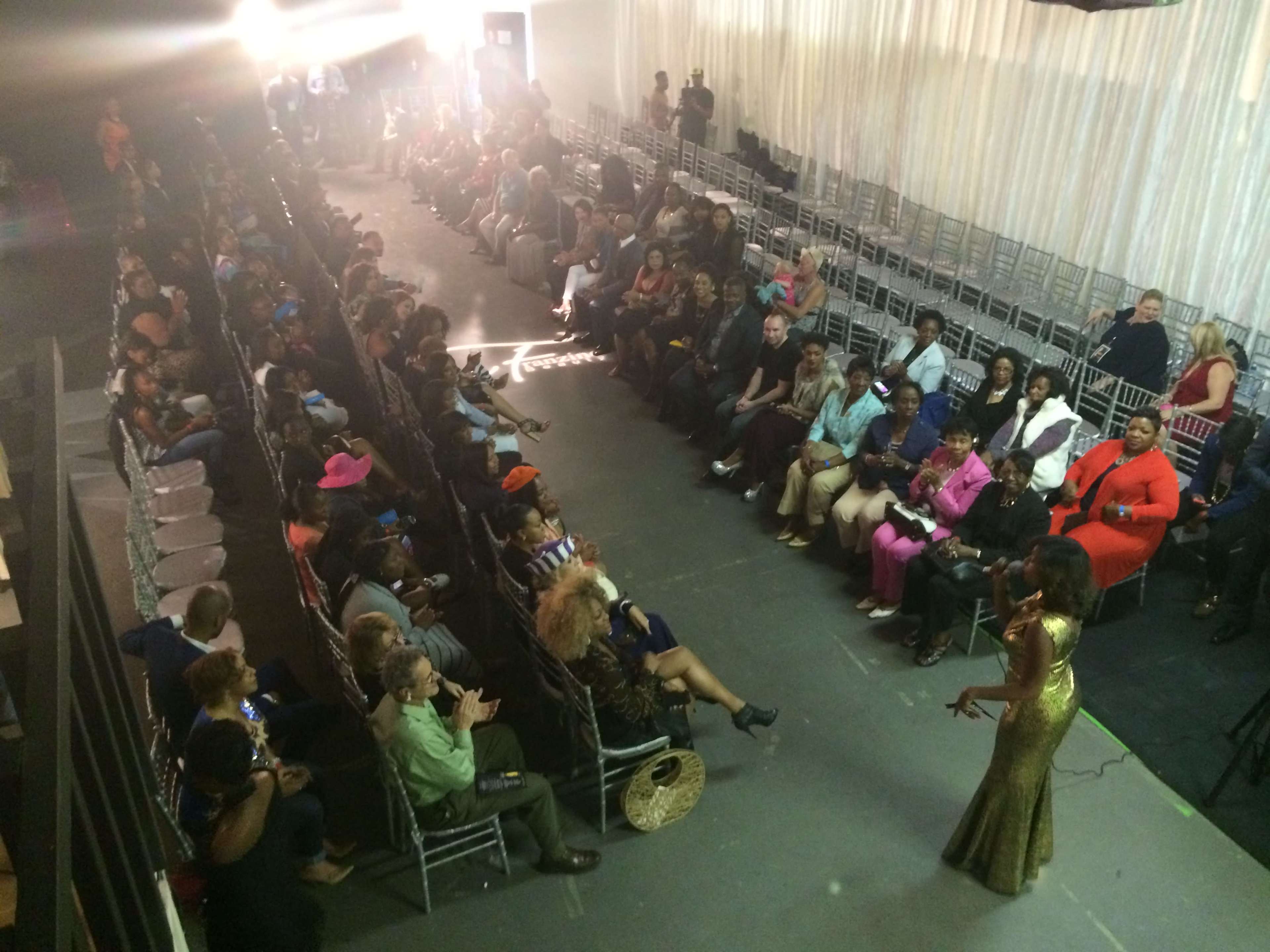 A crowd of seated audience members listens to a speaker at an event in a spacious venue.