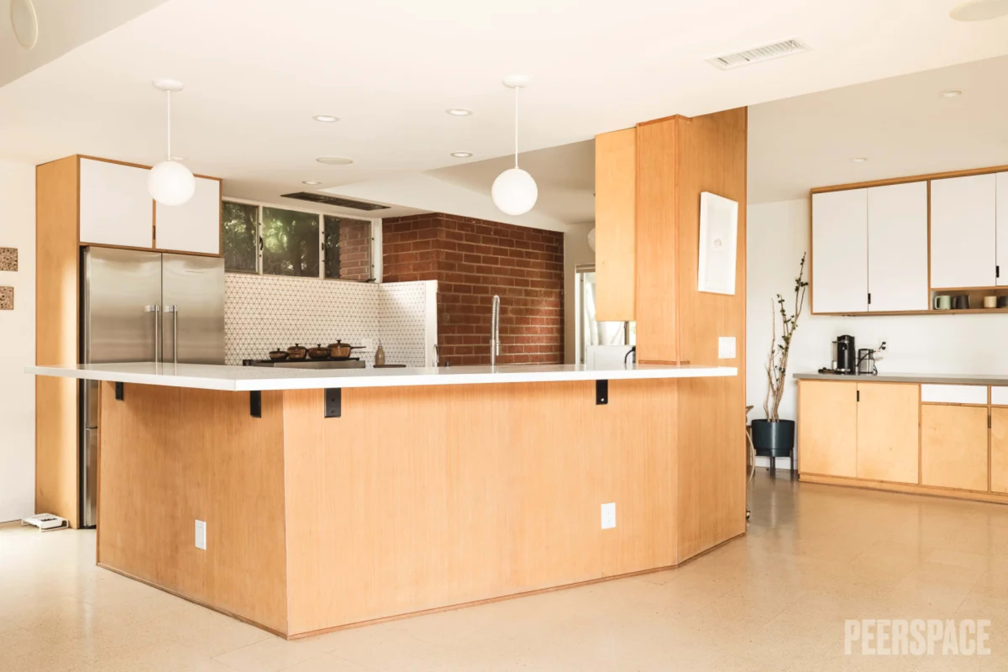 The image shows a modern kitchen with a large island, contemporary cabinetry, and a mix of wooden and white surfaces.