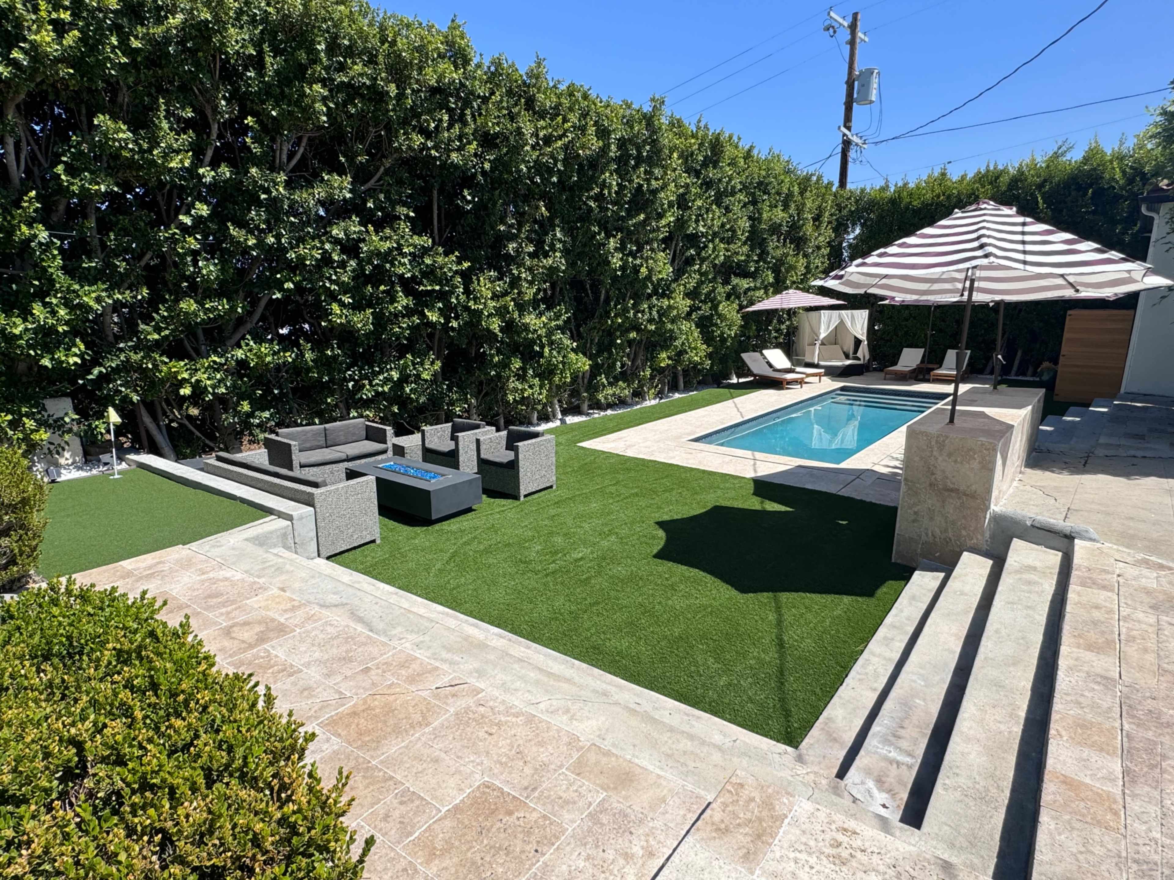 The image shows a backyard with a swimming pool, lounge chairs, a shaded seating area, and landscaped greenery.