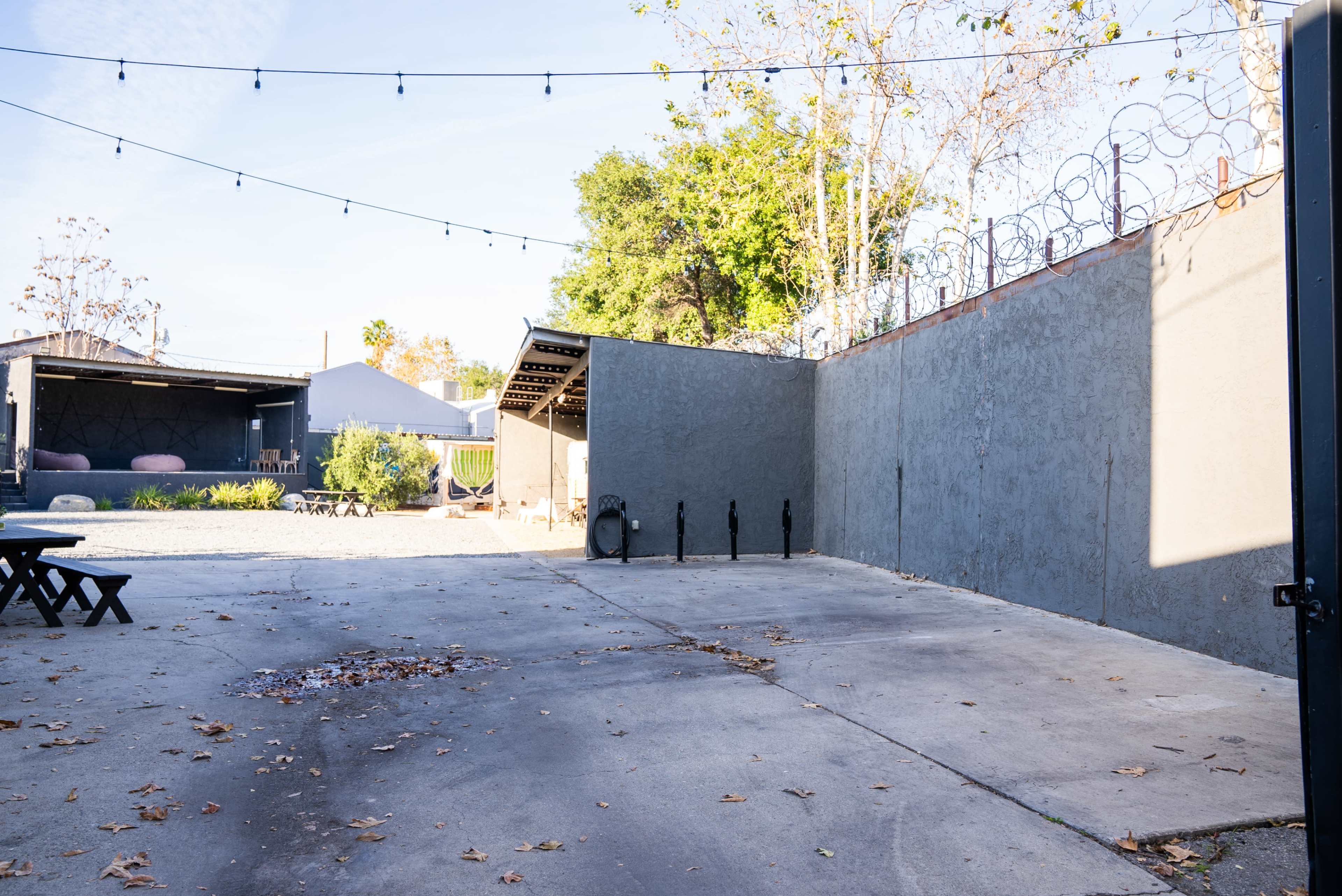 The image shows a spacious outdoor area with a concrete floor, surrounded by walls and string lights overhead, along with some scattered leaves.