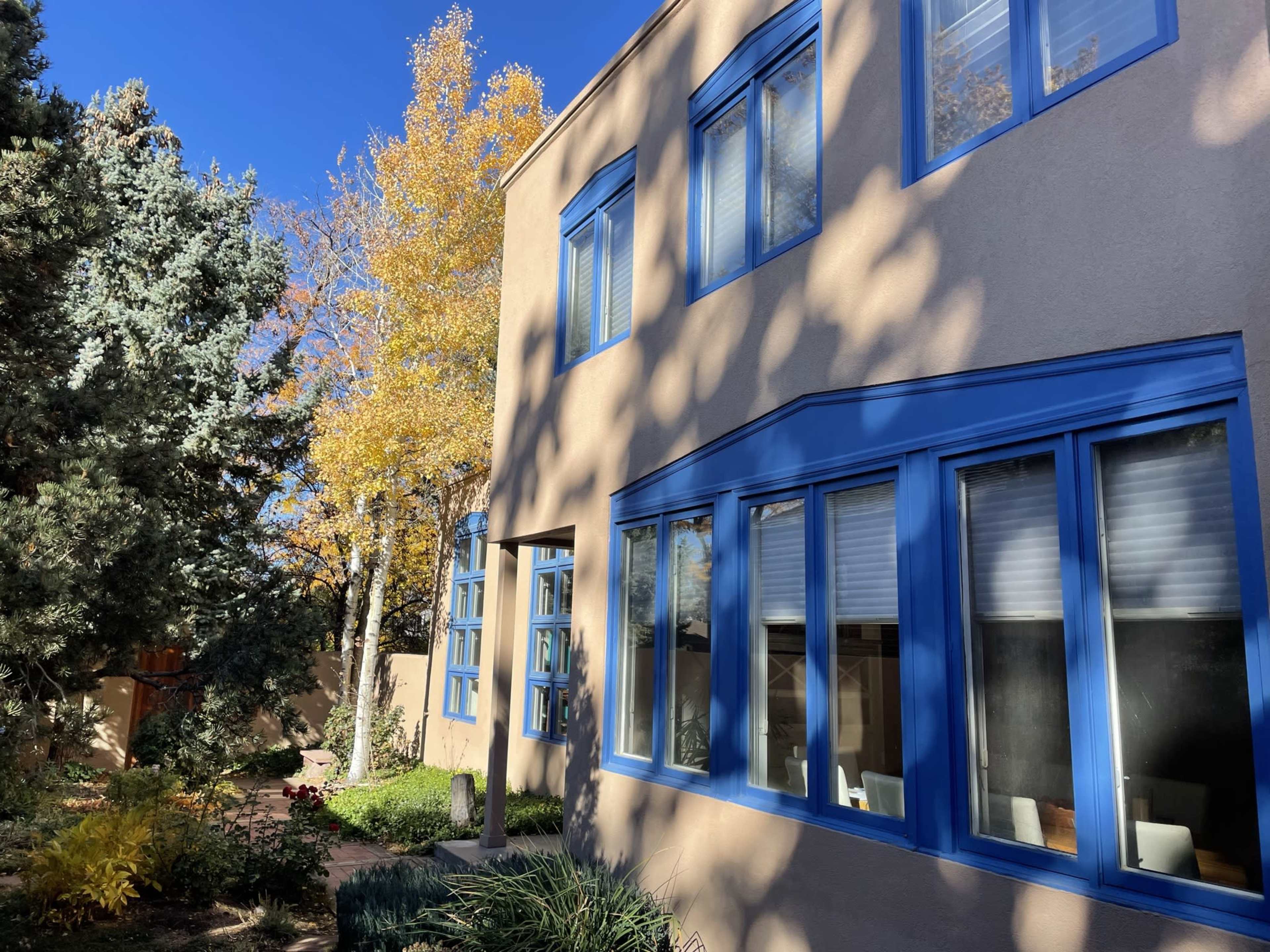 A modern building with blue-trimmed windows is surrounded by trees and colorful foliage.