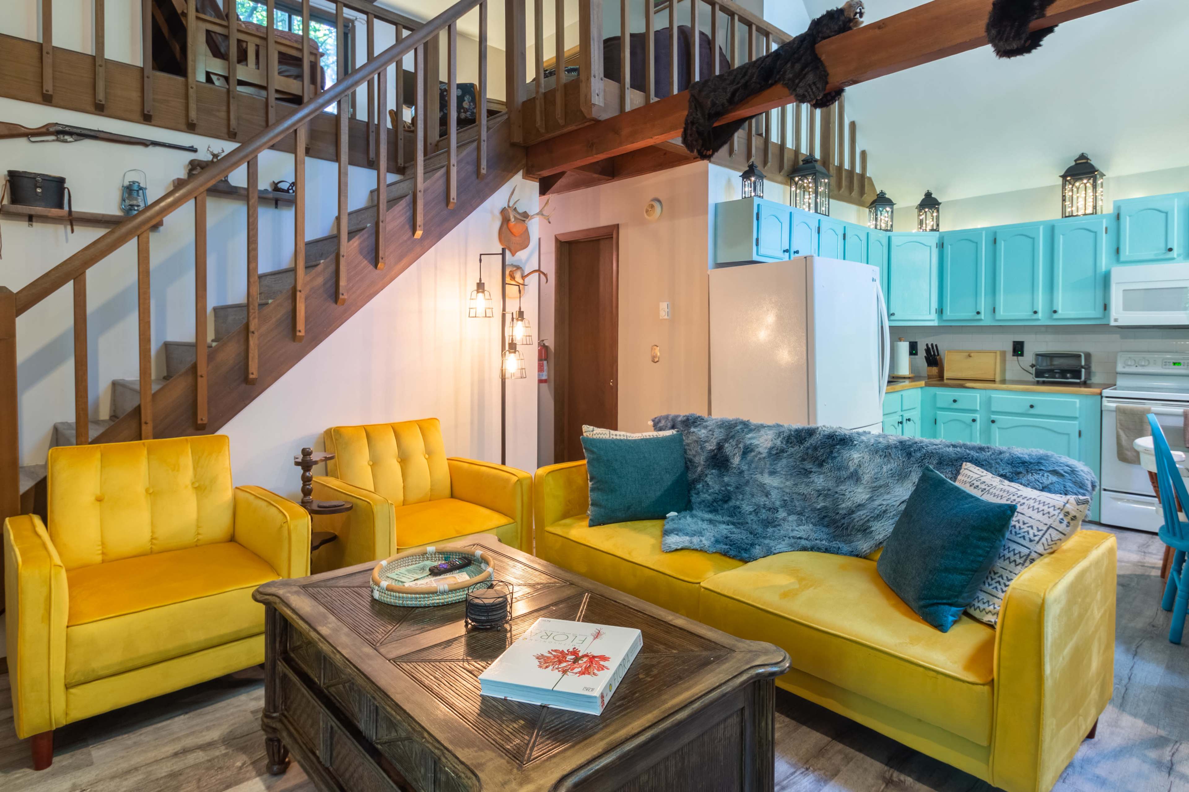 A living room with yellow furniture, a wooden coffee table, and a staircase leading to a loft area.