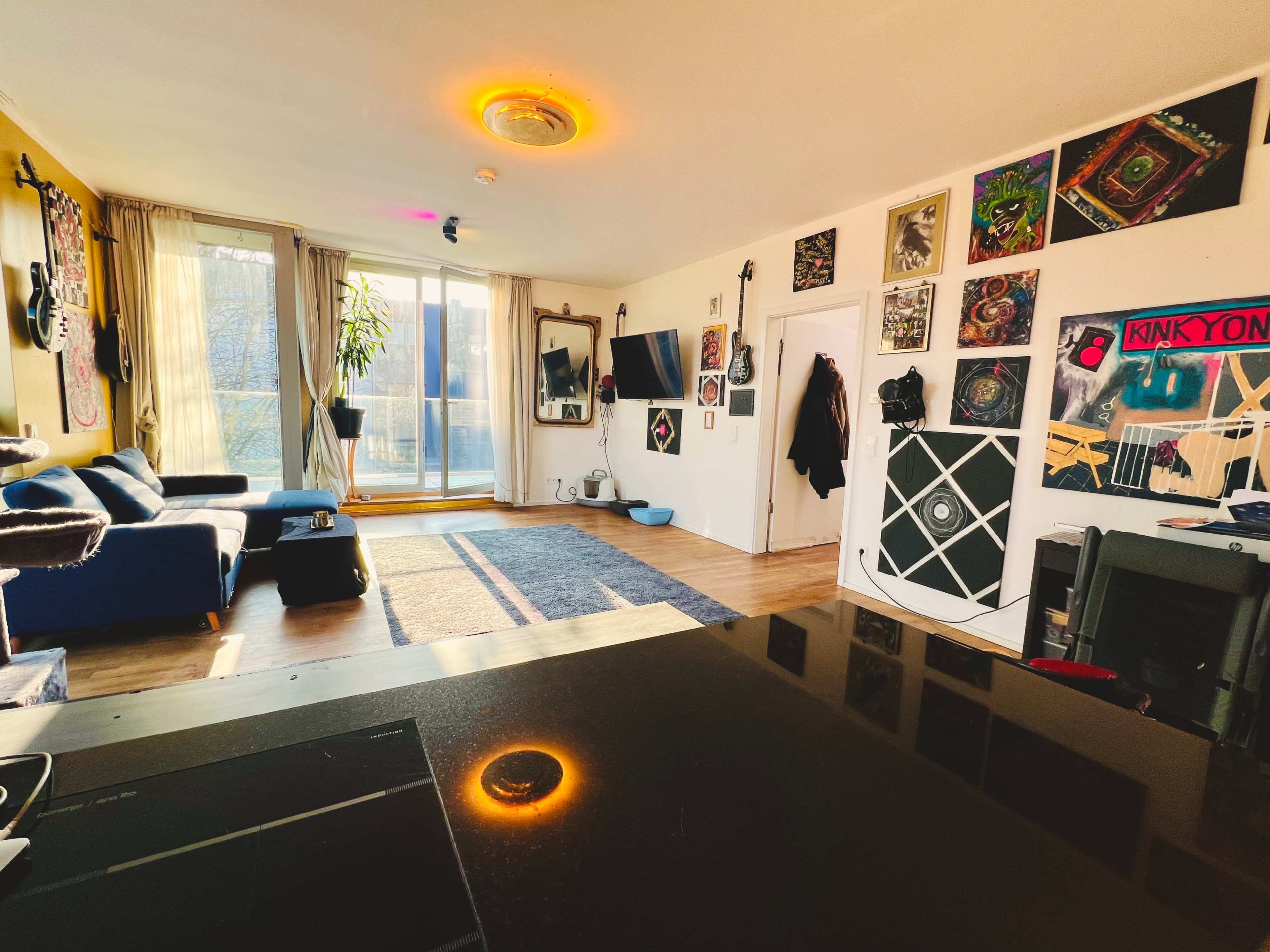 The image shows a brightly lit living room with a blue couch, a large window, a flat-screen TV, and colorful wall art.