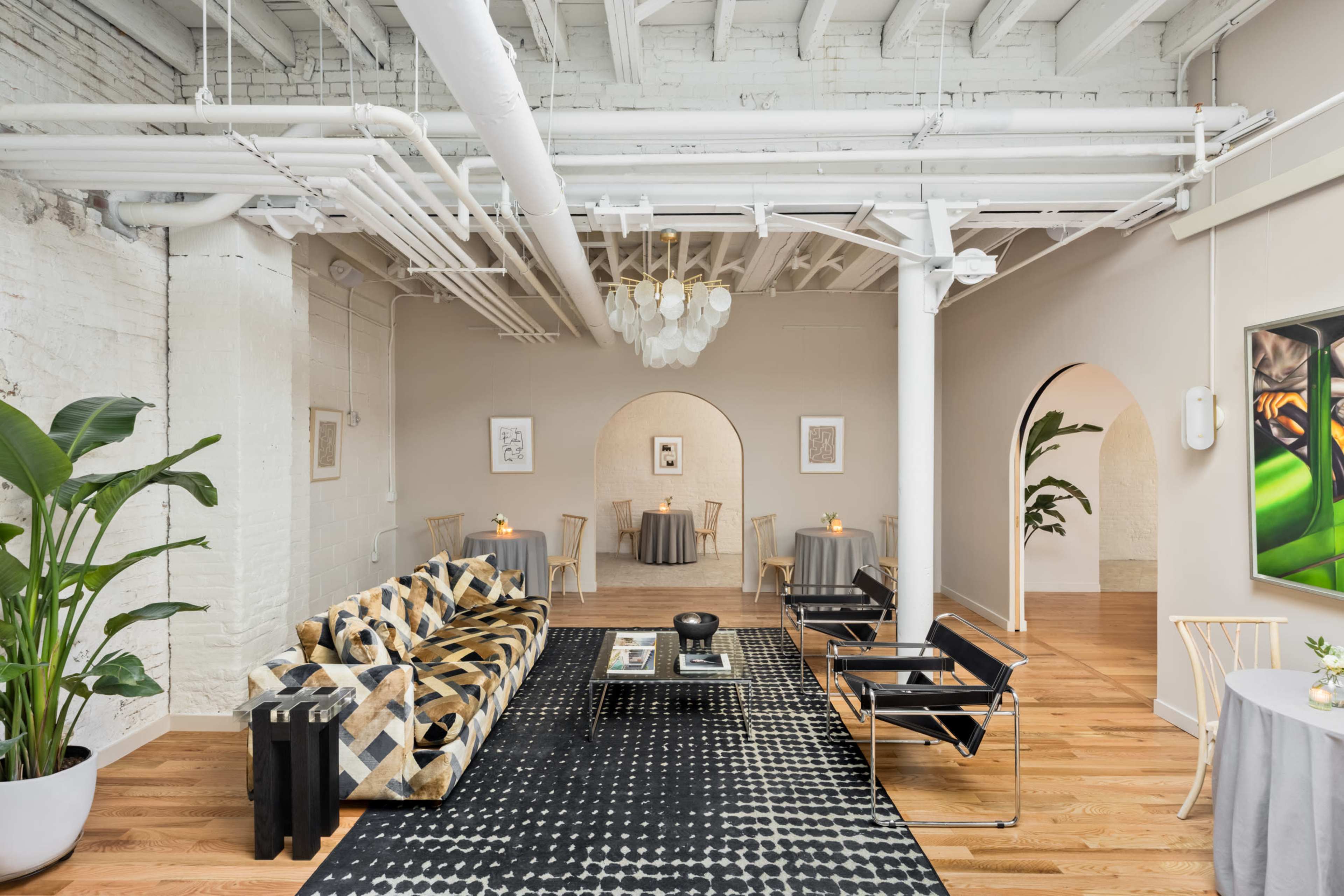 A stylish interior of a spacious room with a patterned sofa, minimalist furniture, and soft lighting, featuring archways and plants.