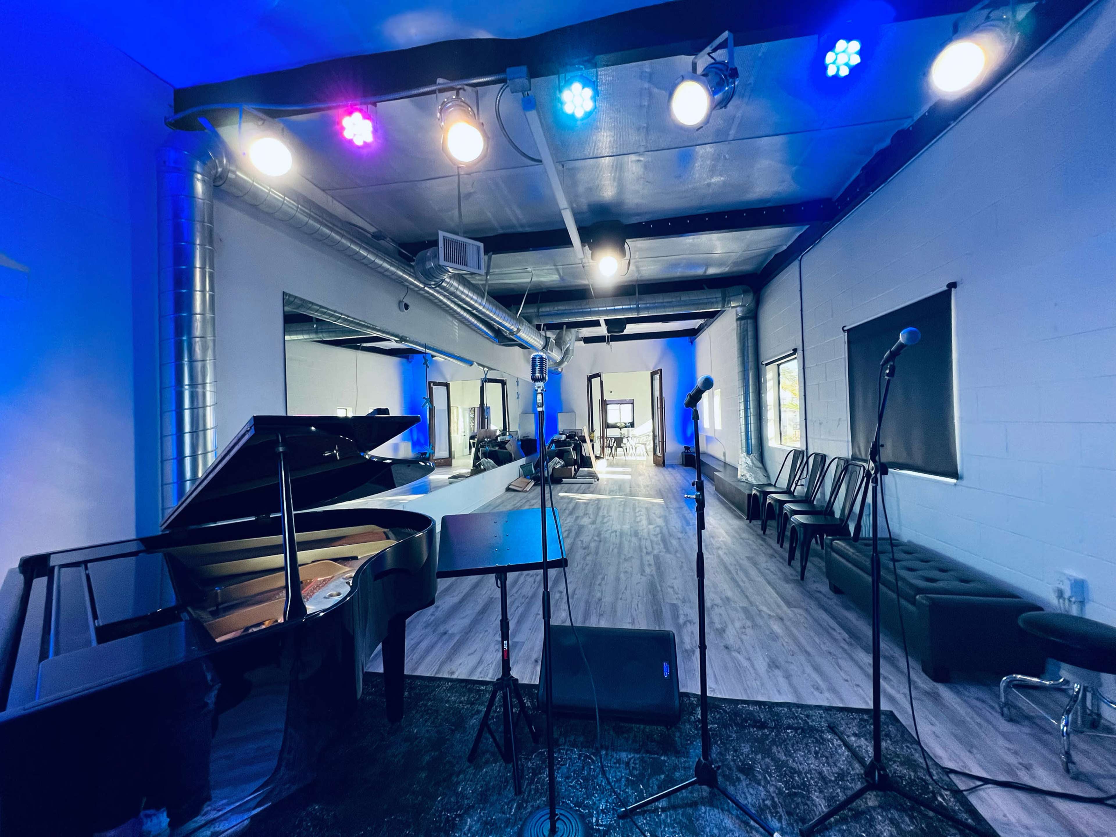 A music rehearsal space with a grand piano, microphone stands, and rows of chairs arranged against the wall.