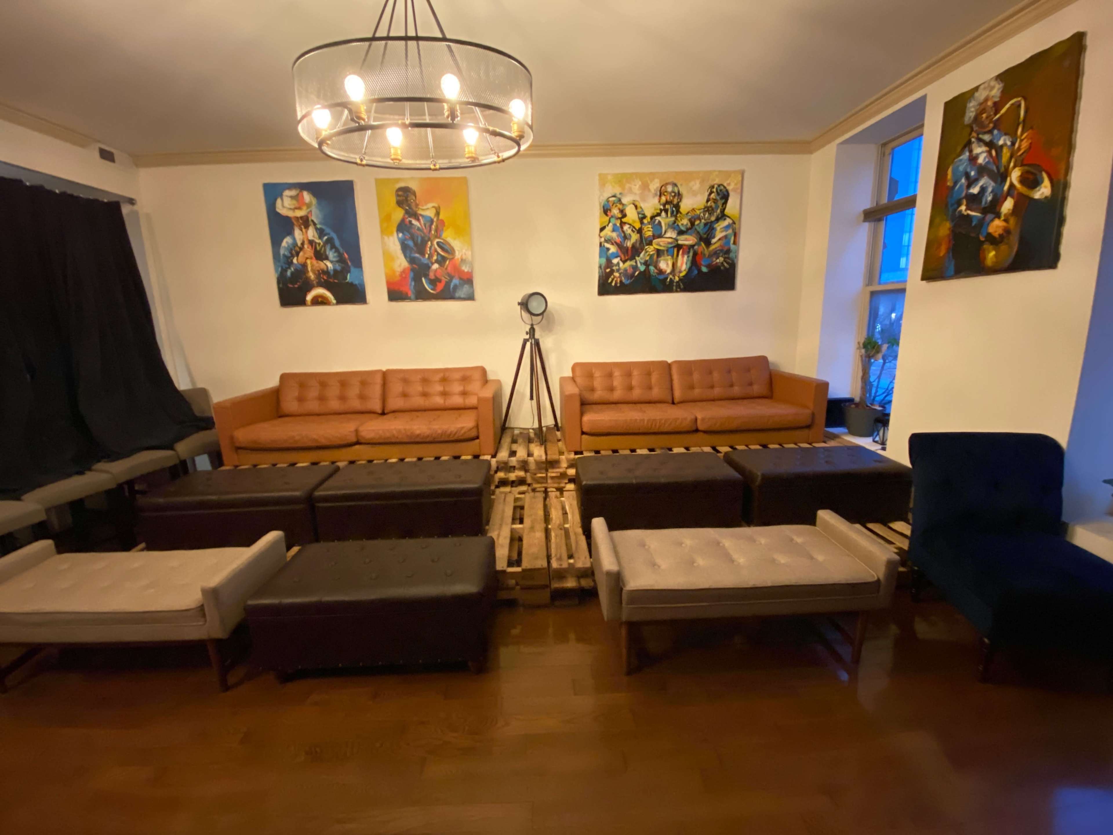 The room features a set of brown and gray couches arranged around wooden pallet tables, with large colorful paintings on the wall.