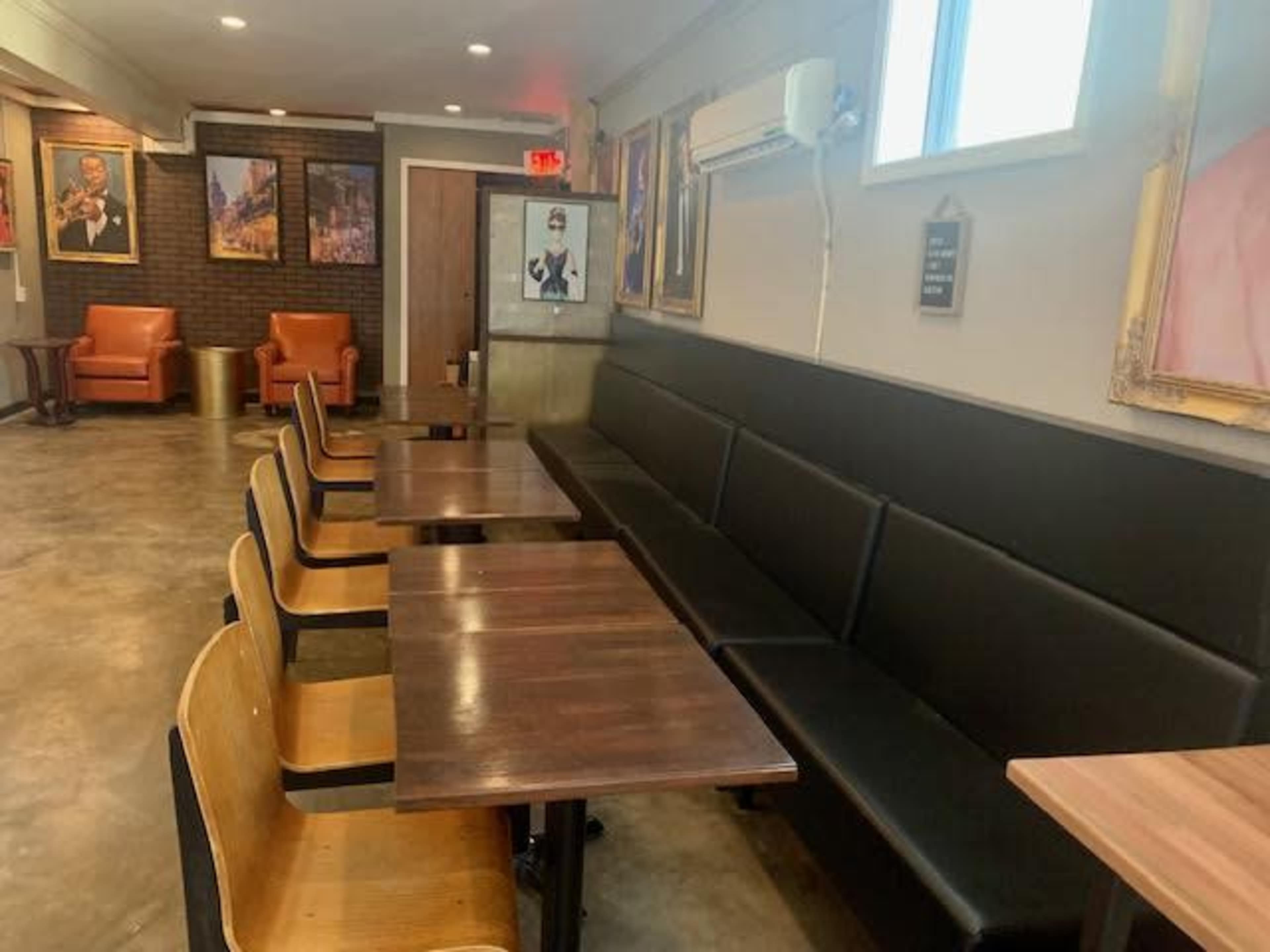 The image shows a café interior with a row of black benches and wooden tables, complemented by framed artworks on the walls.