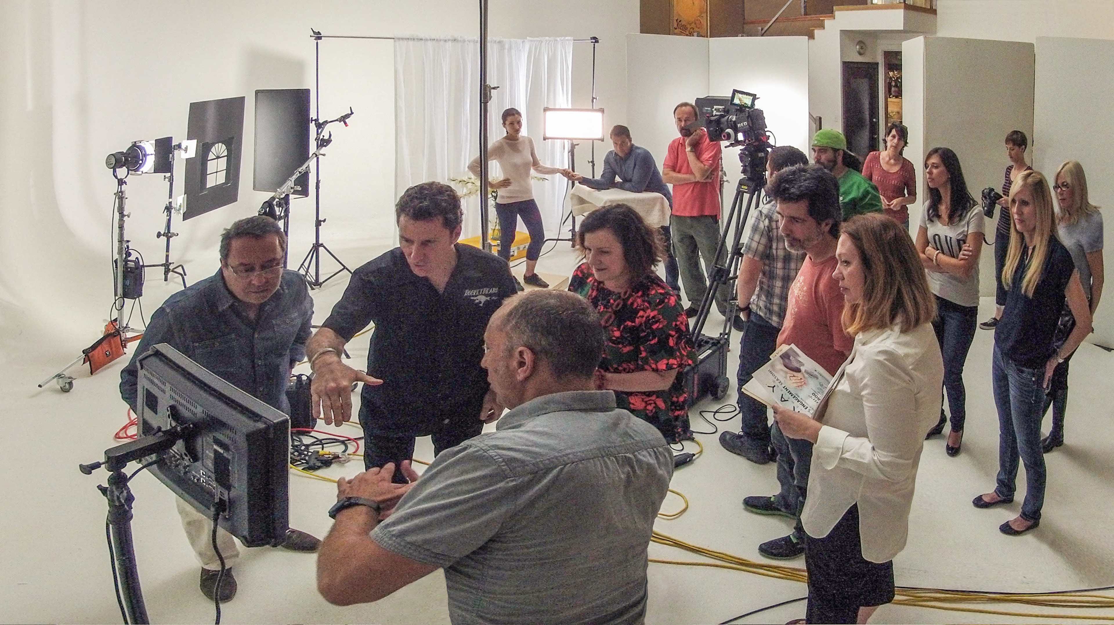 A group of people collaborates around a monitor on a film set, with various cameras and equipment visible in the background.