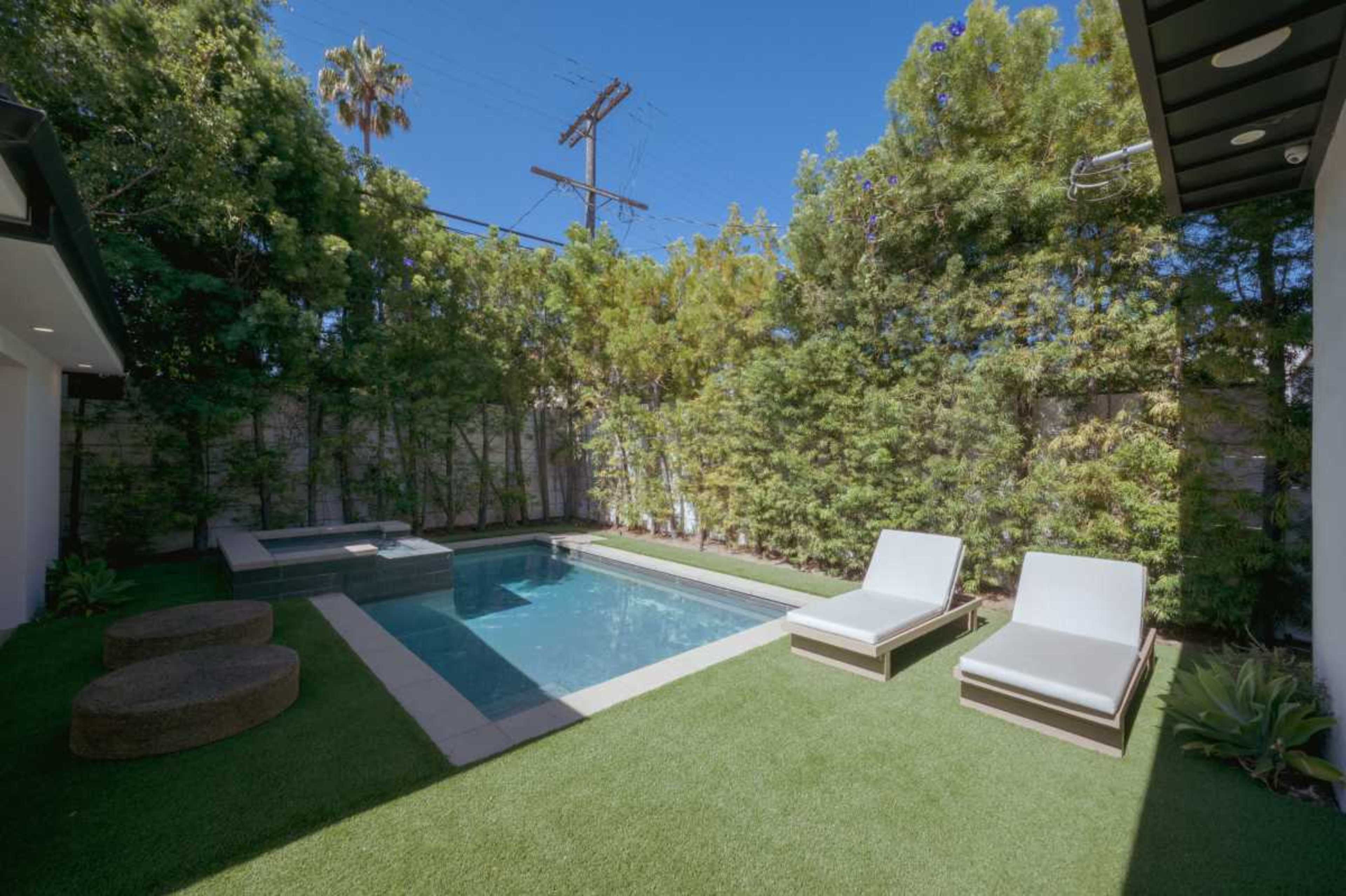 A small pool area features a rectangular pool surrounded by greenery and two tan lounge chairs on artificial grass.