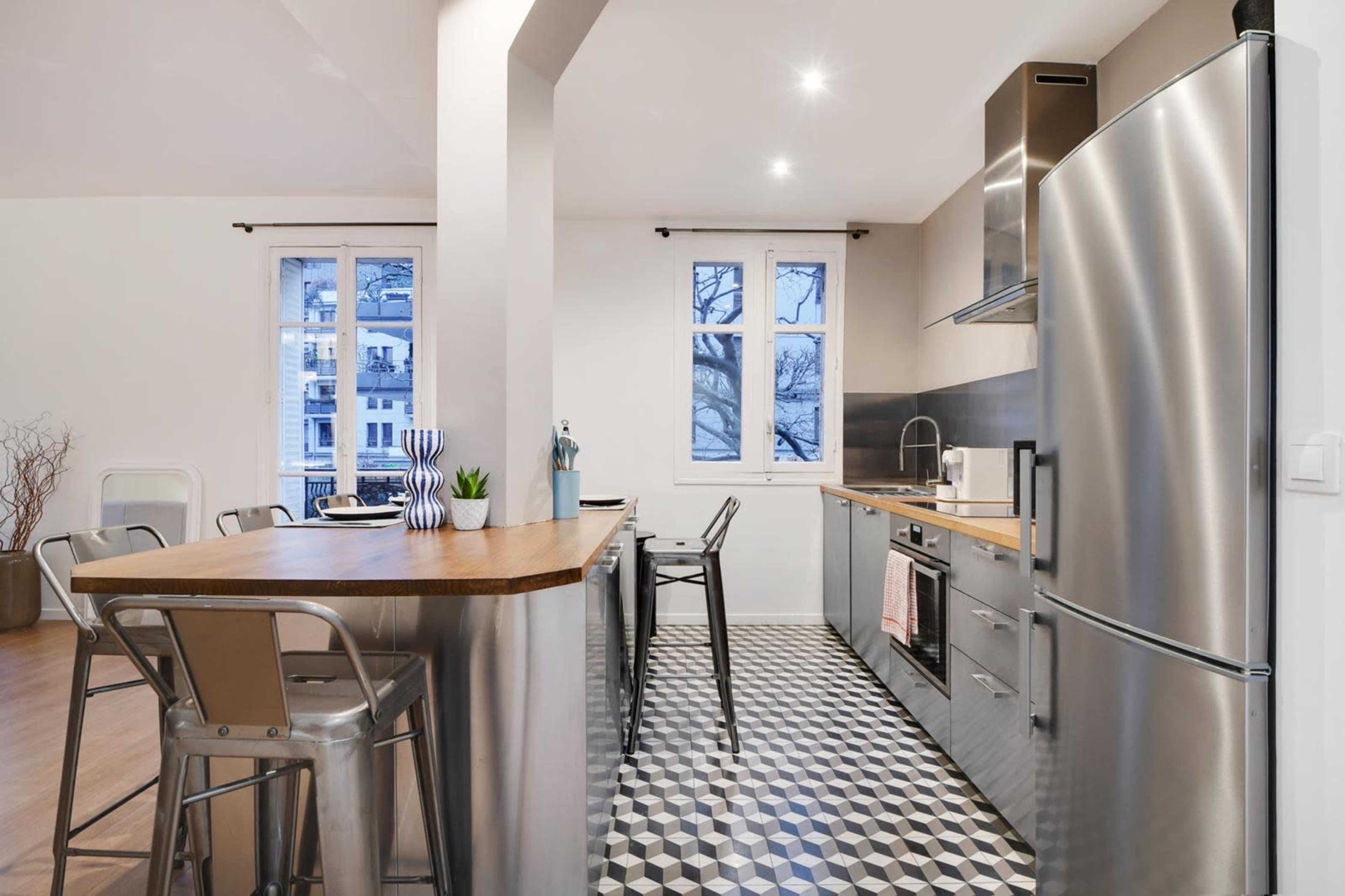 A modern kitchen with stainless steel appliances, a wooden countertop, and a patterned tile floor.