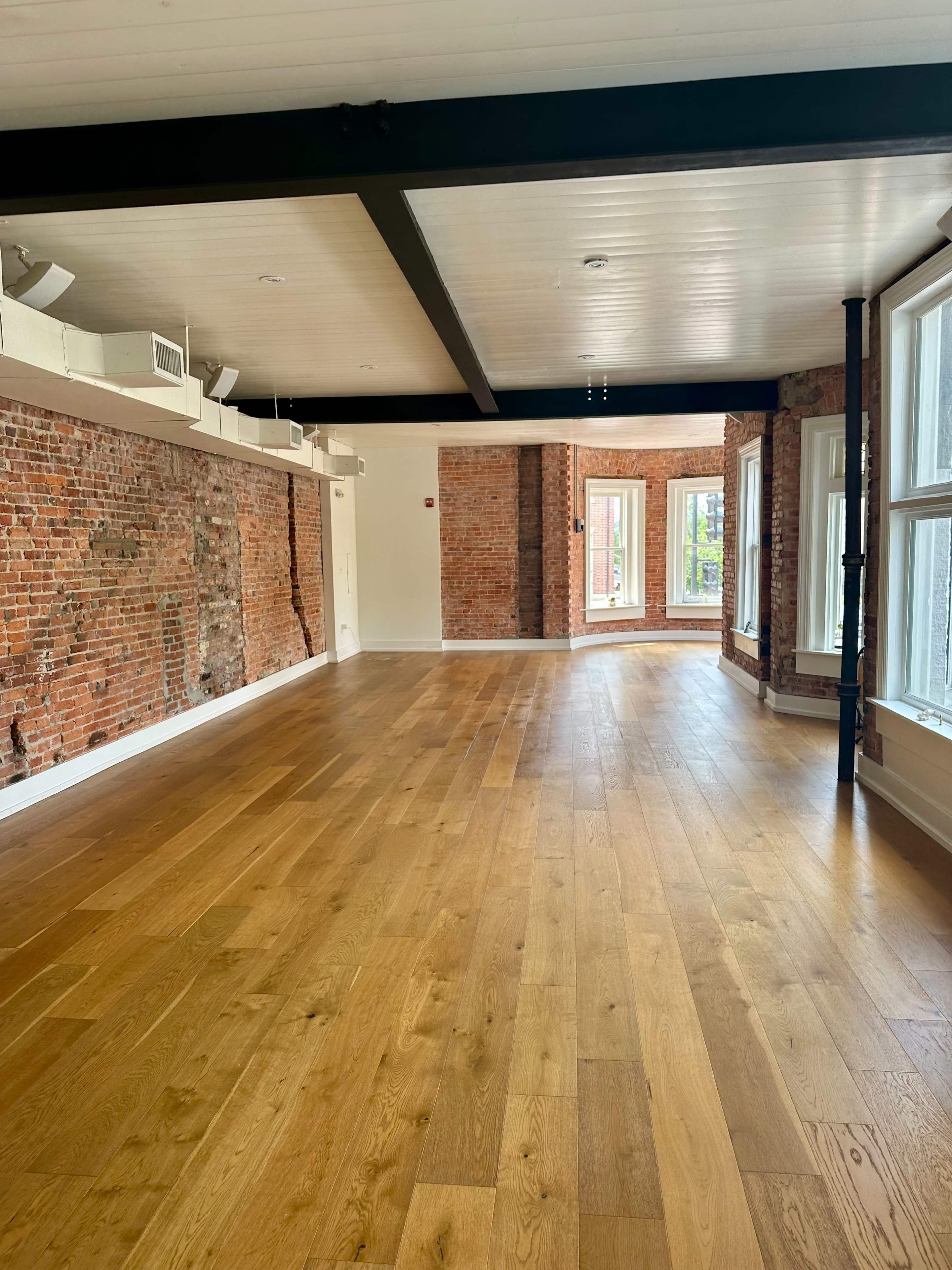 The image shows an open room with exposed brick walls and wood flooring.