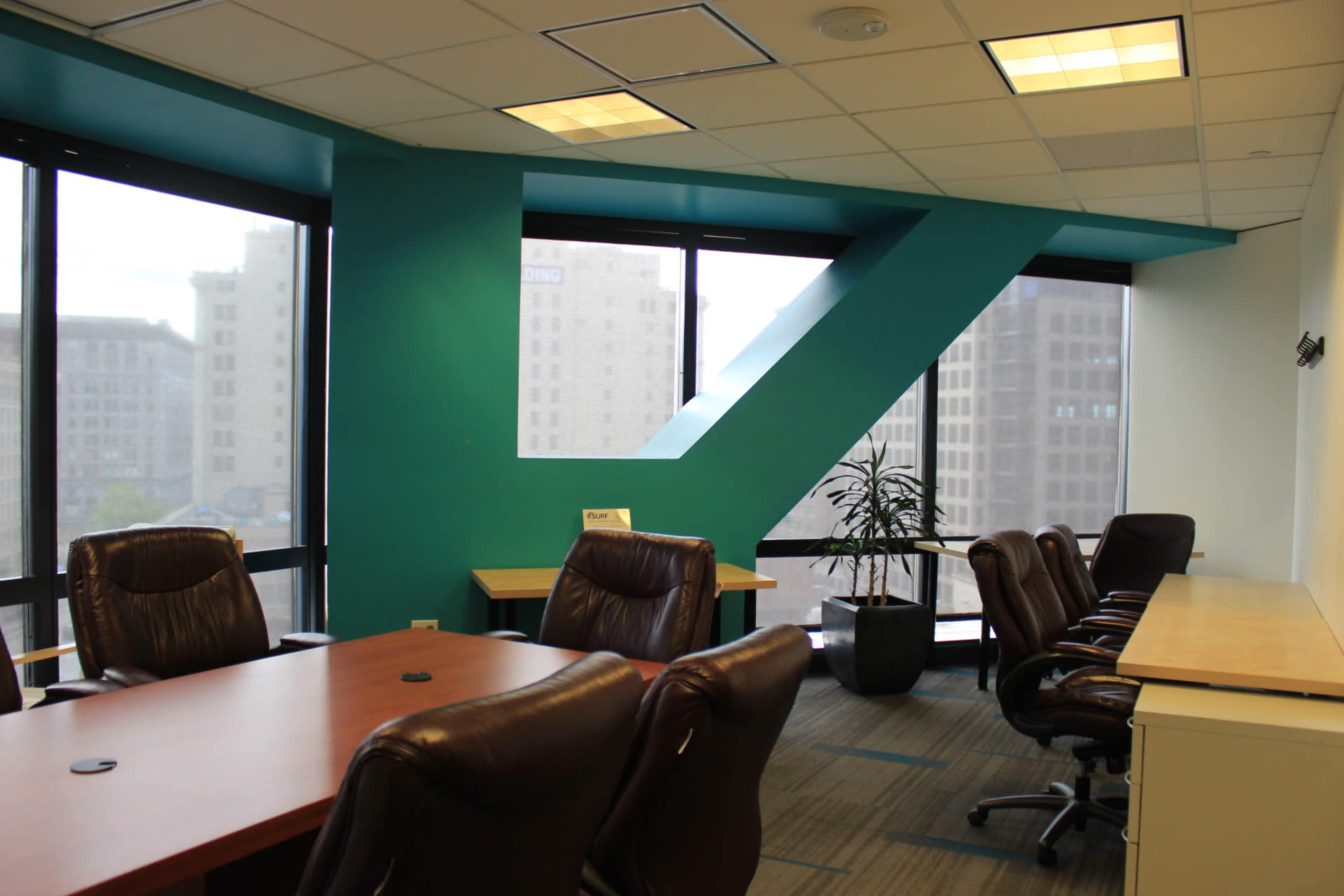 A modern office conference room with a large wooden table, ergonomic chairs, and large windows overlooking a cityscape.