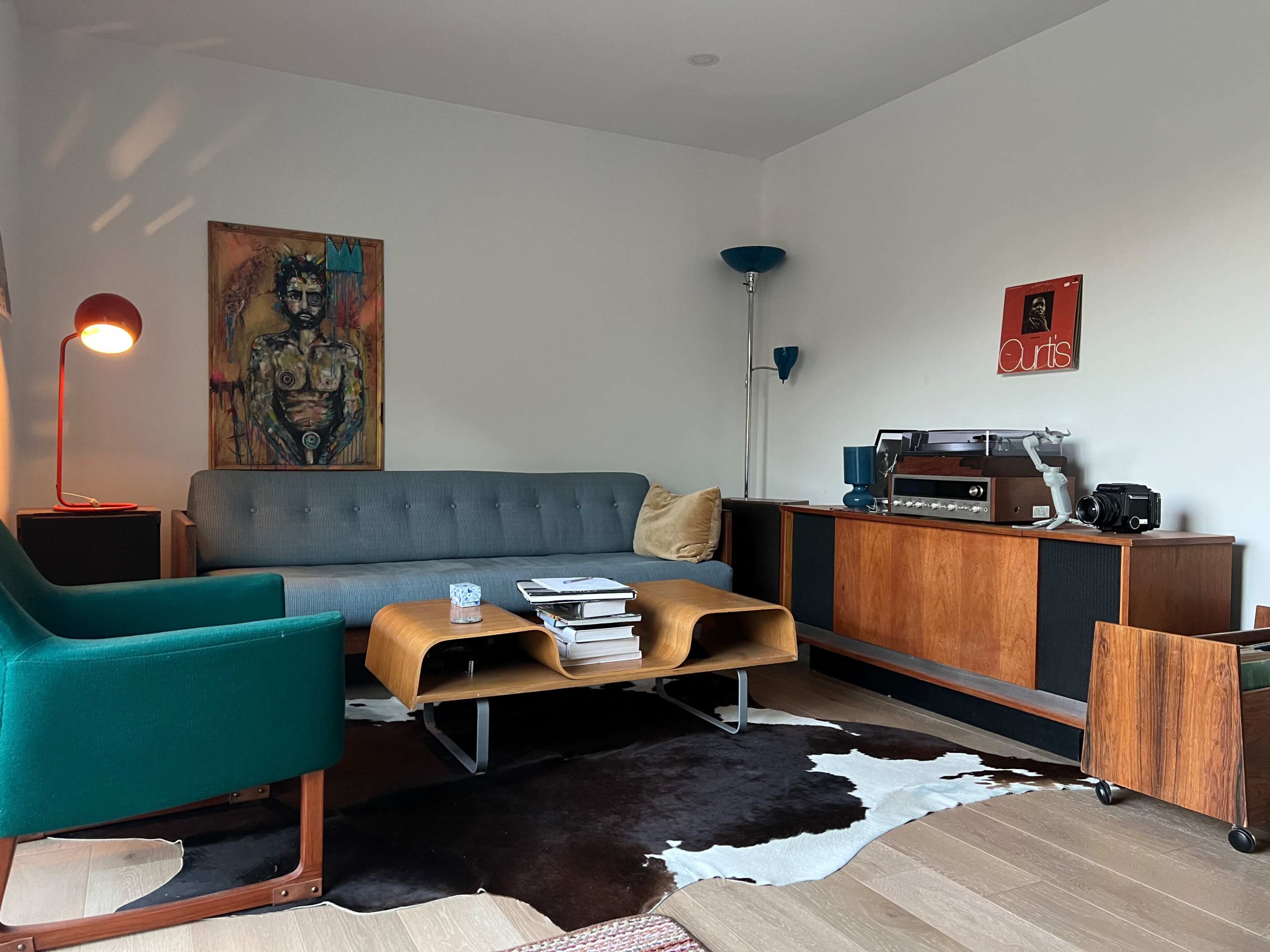 A modern living room with a gray sofa, a green armchair, a mid-century wooden coffee table, and a vintage stereo system on a wooden console, all arranged on a cowhide rug.
