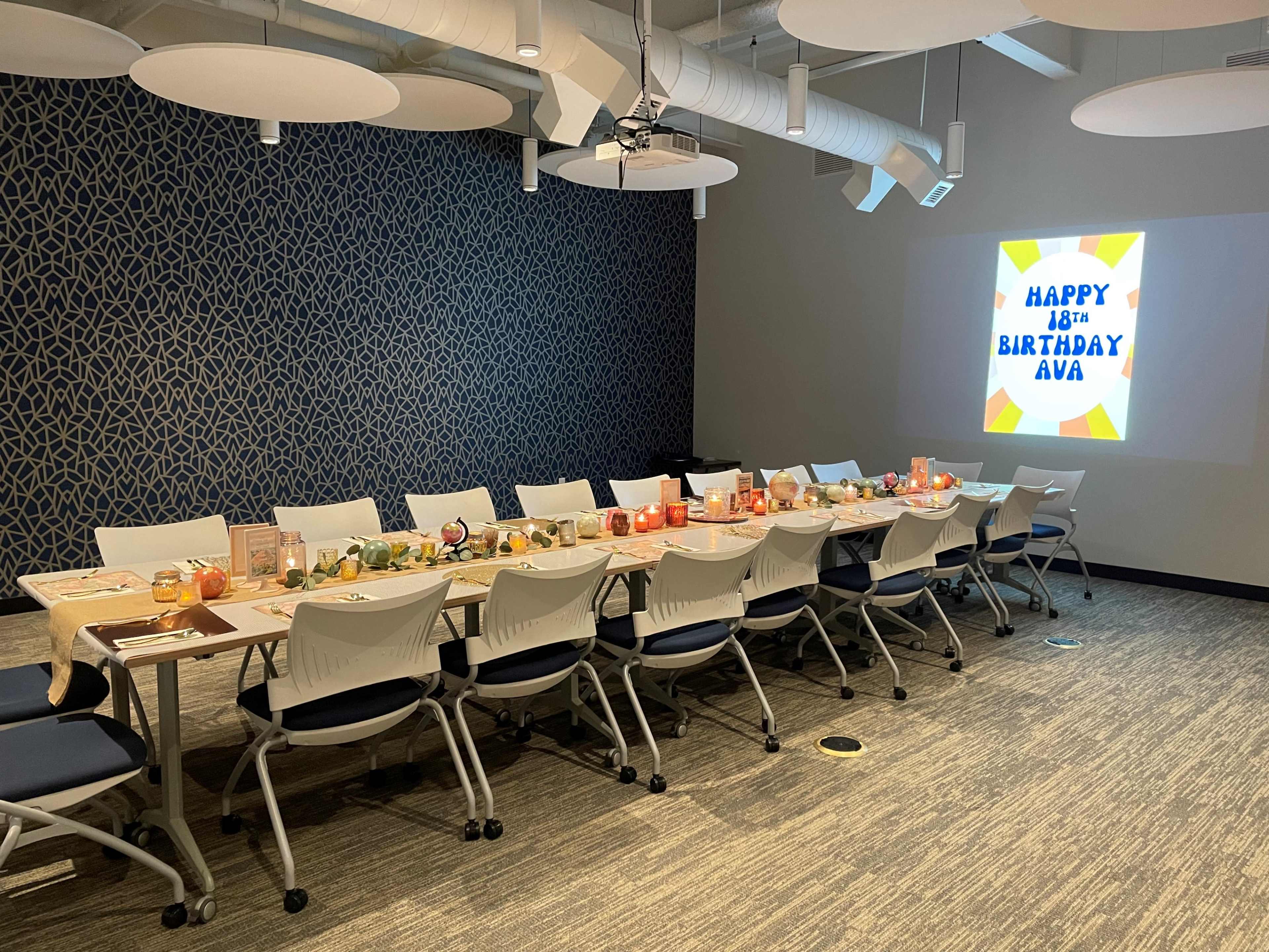 A long table is set with decorations and food in a room, with a wall displaying a "Happy 18th Birthday Ava" banner.