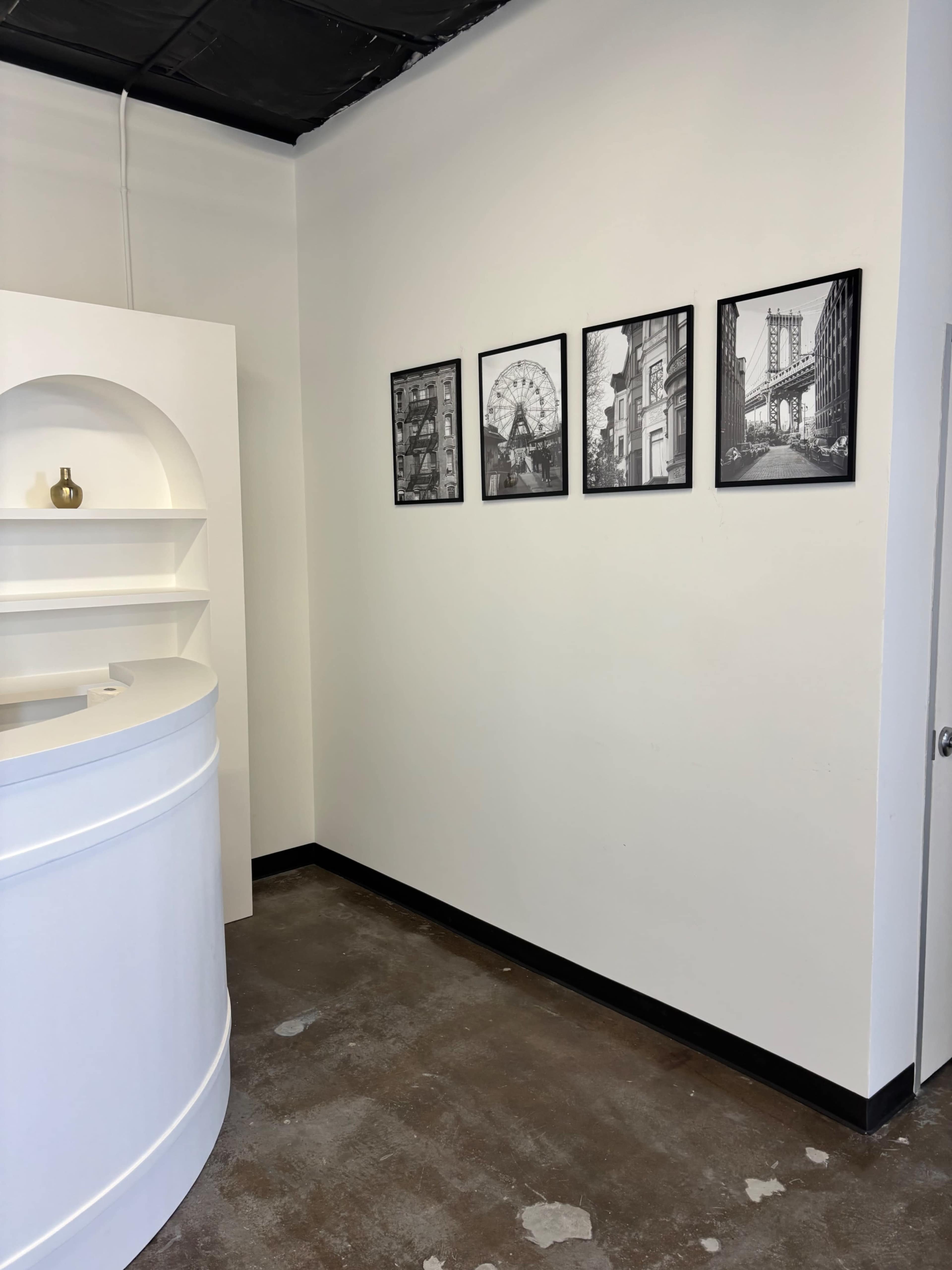 The image shows a clean, minimalist interior with a white curved reception desk and four black-and-white framed photographs mounted on the wall.