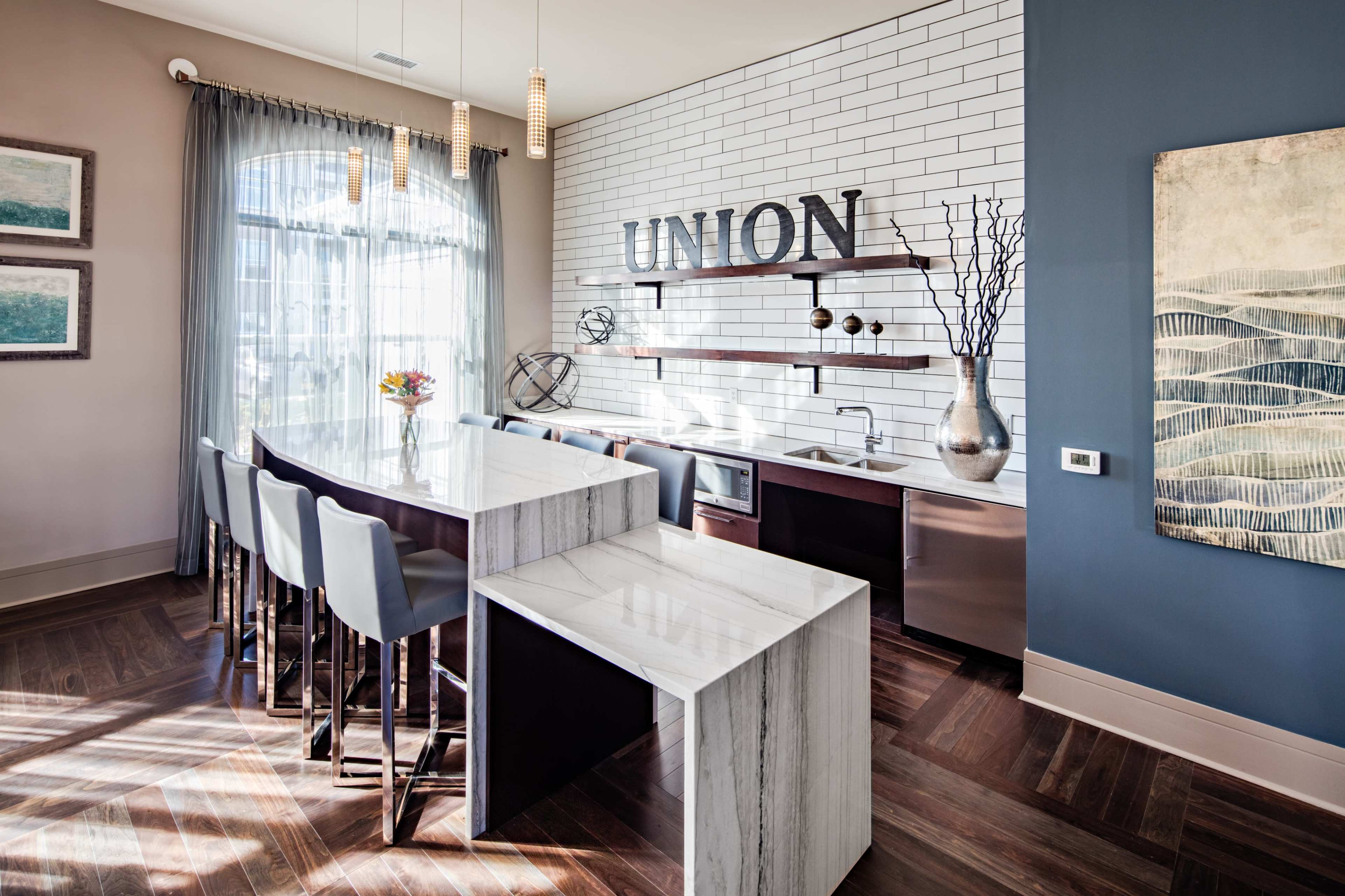 A modern kitchen area with a marble countertop, high chairs, and a wall featuring the word "UNION" in large lettering, accompanied by shelves and decorative elements.