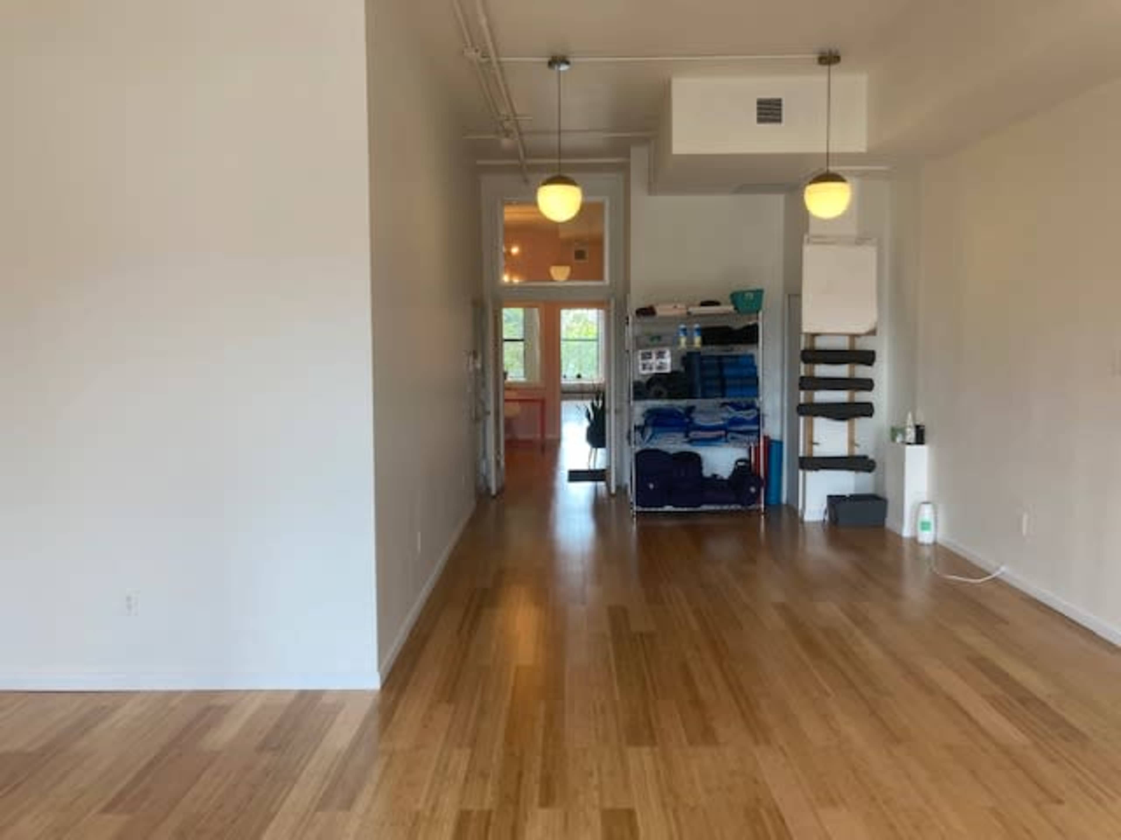 A spacious room with wooden flooring, bright lighting, and a shelf stacked with blue towels at the back.