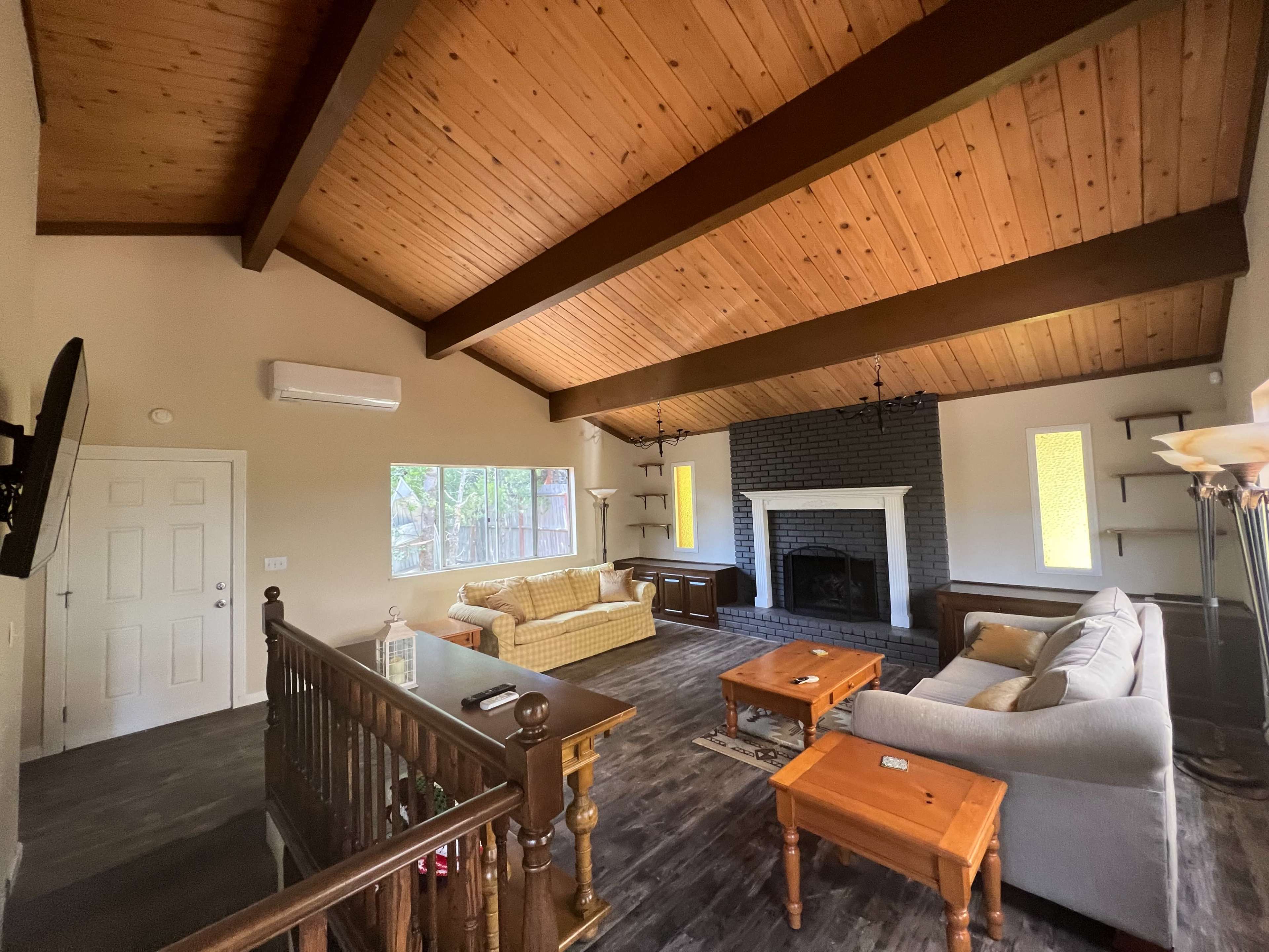 The living room features a vaulted wooden ceiling, exposed beams, two sofas, a coffee table, and a fireplace against a dark brick wall.