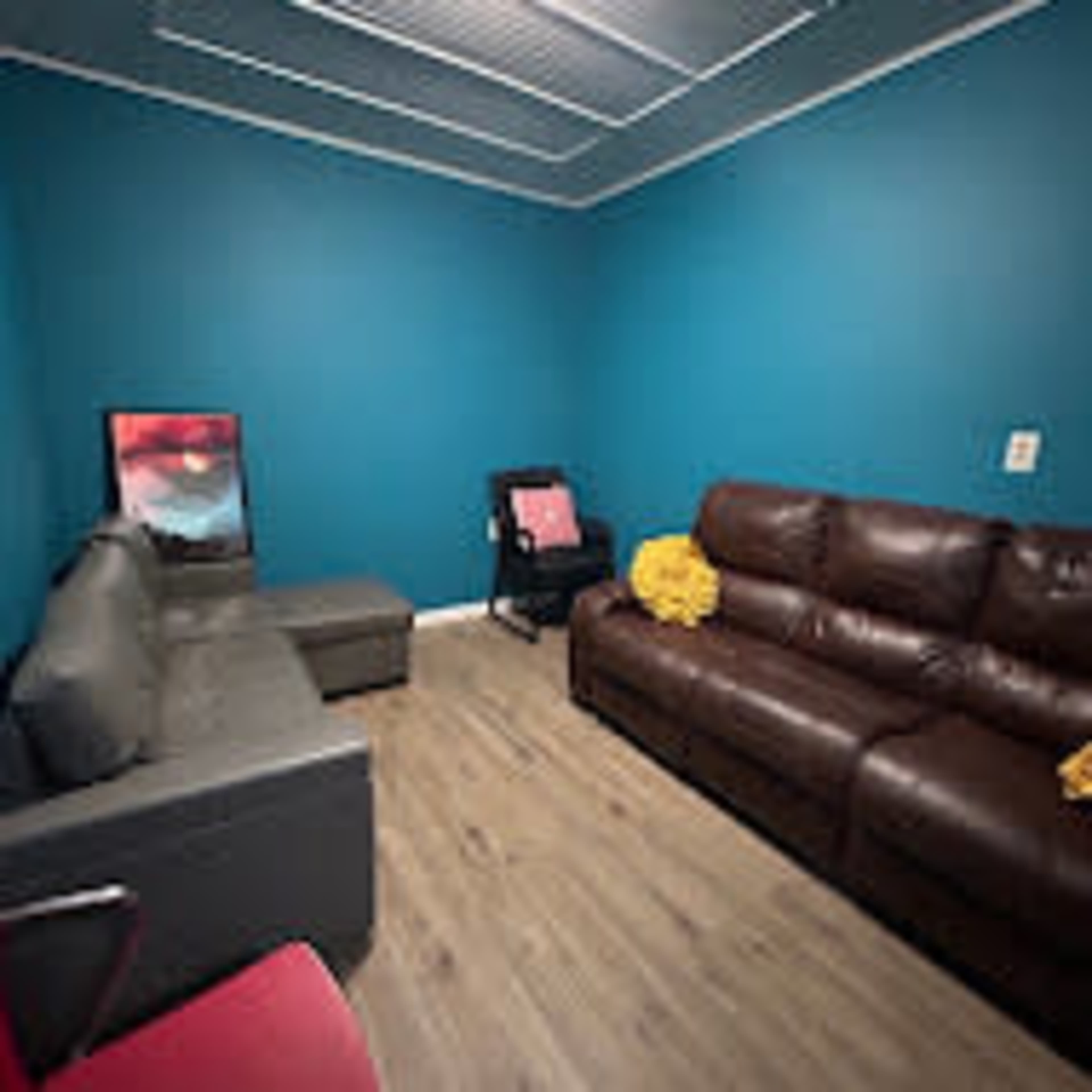 A small room featuring a brown leather sofa, a gray couch, a chair, and blue walls.