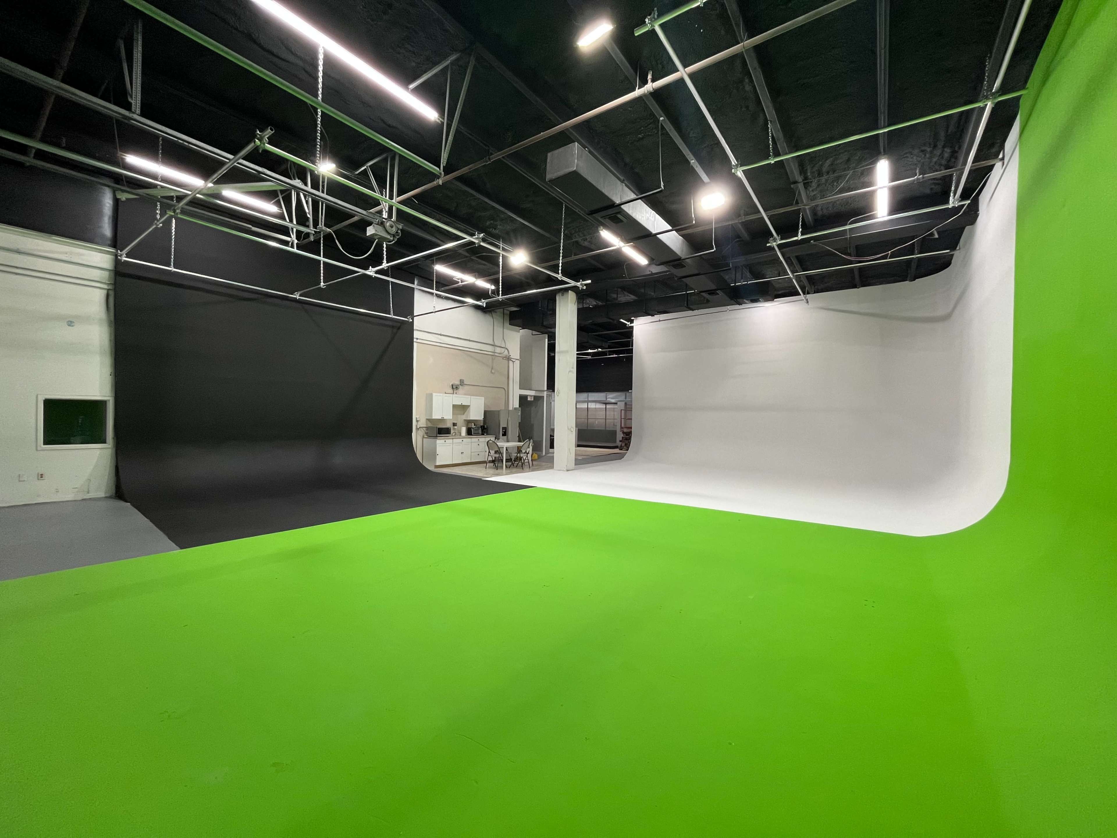 The image shows a spacious photography studio featuring a green, black, and white seamless backdrop.