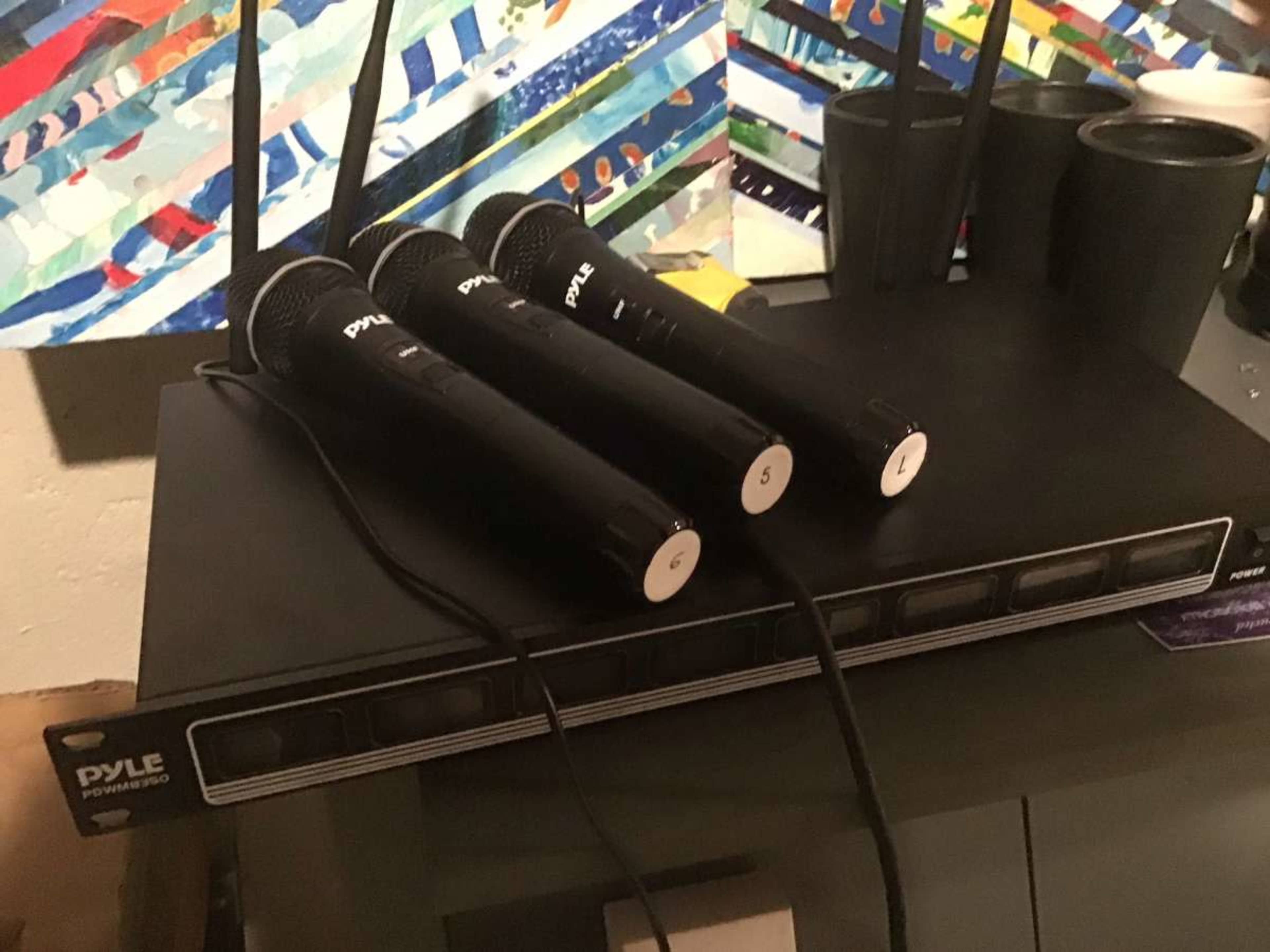 The image shows three wireless microphones resting on a black Pyle receiver with multiple buttons and antennas.