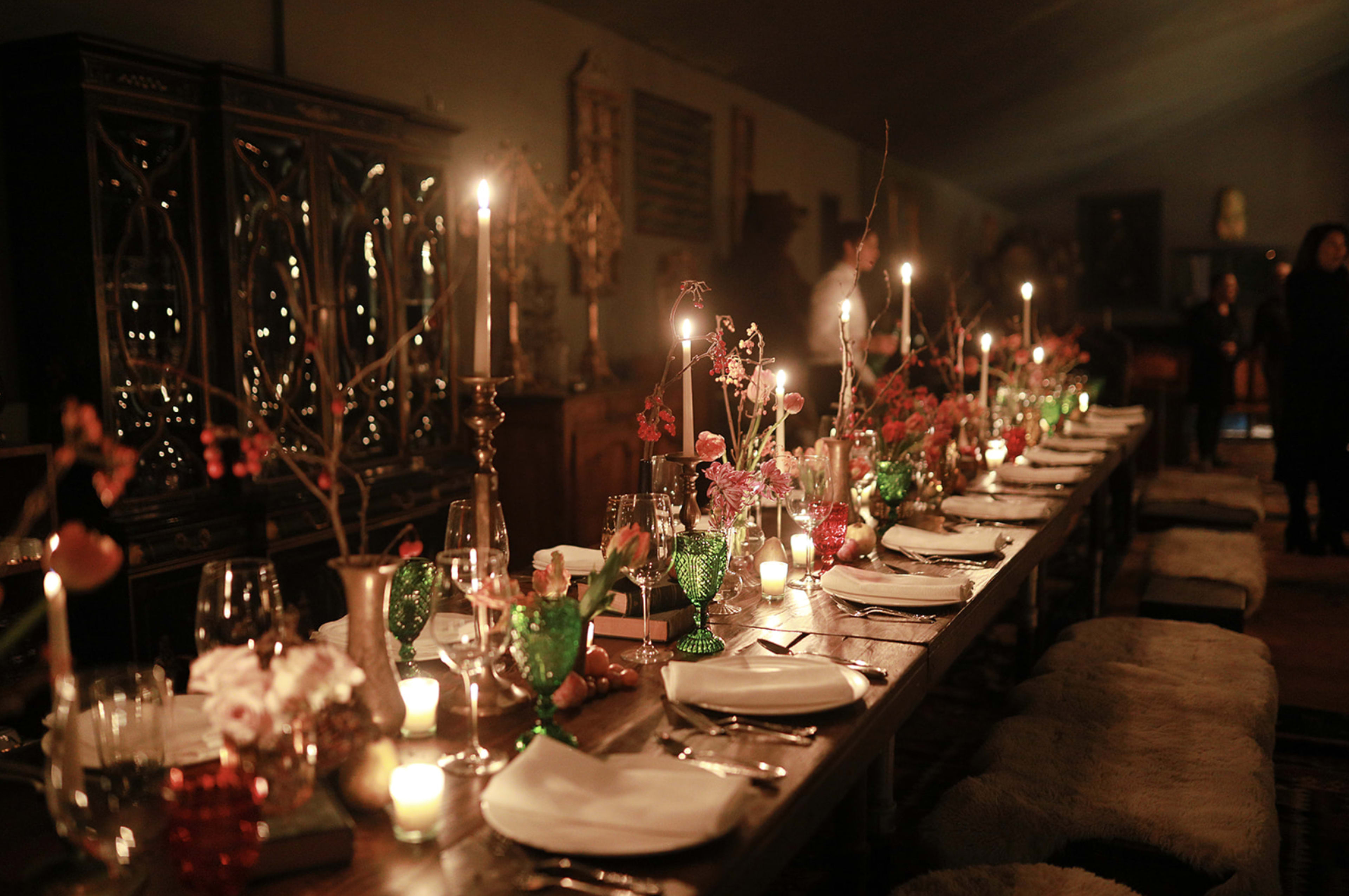 A long dining table is elegantly set with candles, glassware, and floral arrangements in a dimly lit room.
