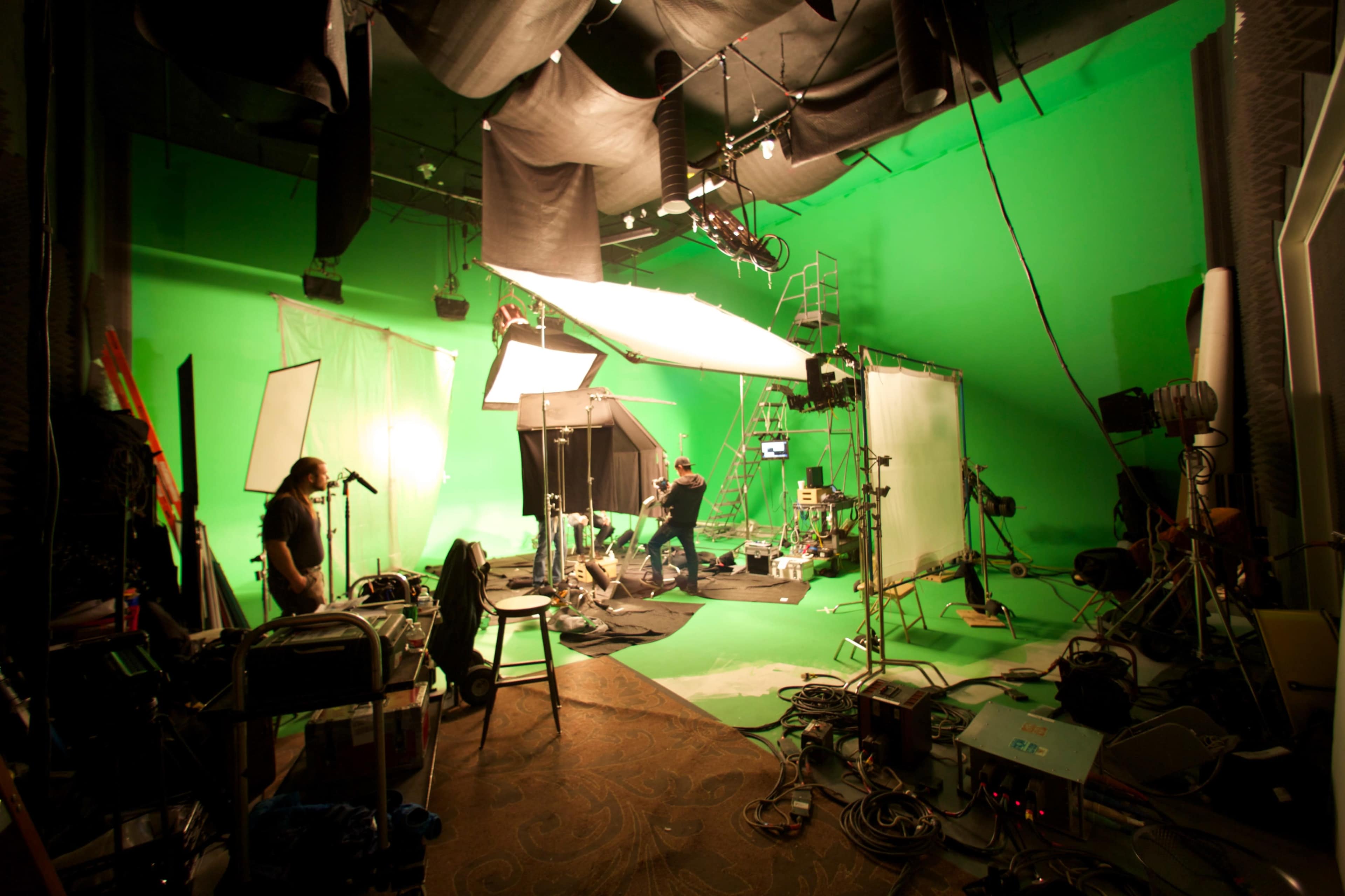 A film studio scene shows crew members setting up equipment on a green screen backdrop.