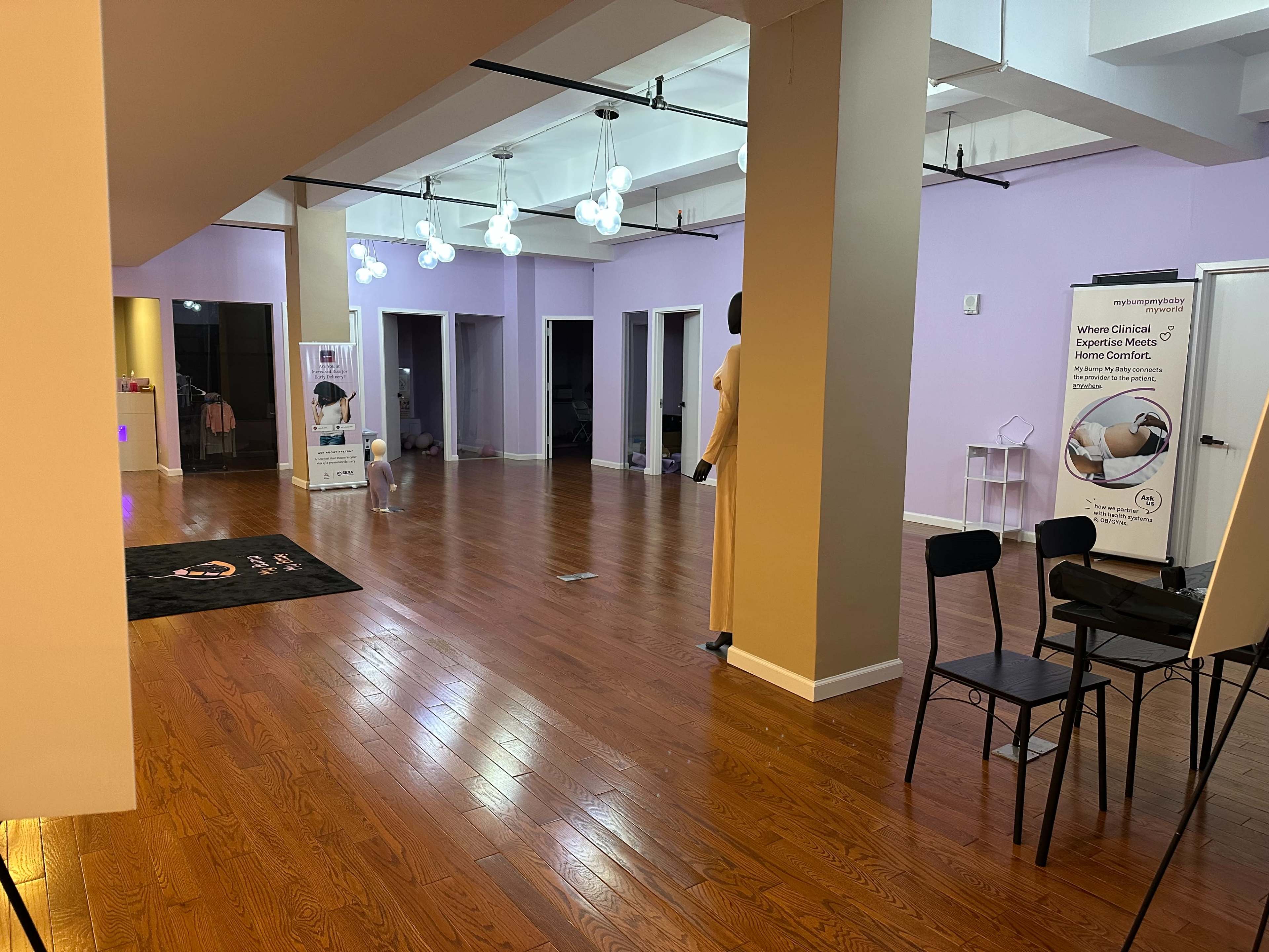 The image shows a spacious room with hardwood flooring, purple walls, several doors, and soft lighting from hanging fixtures.