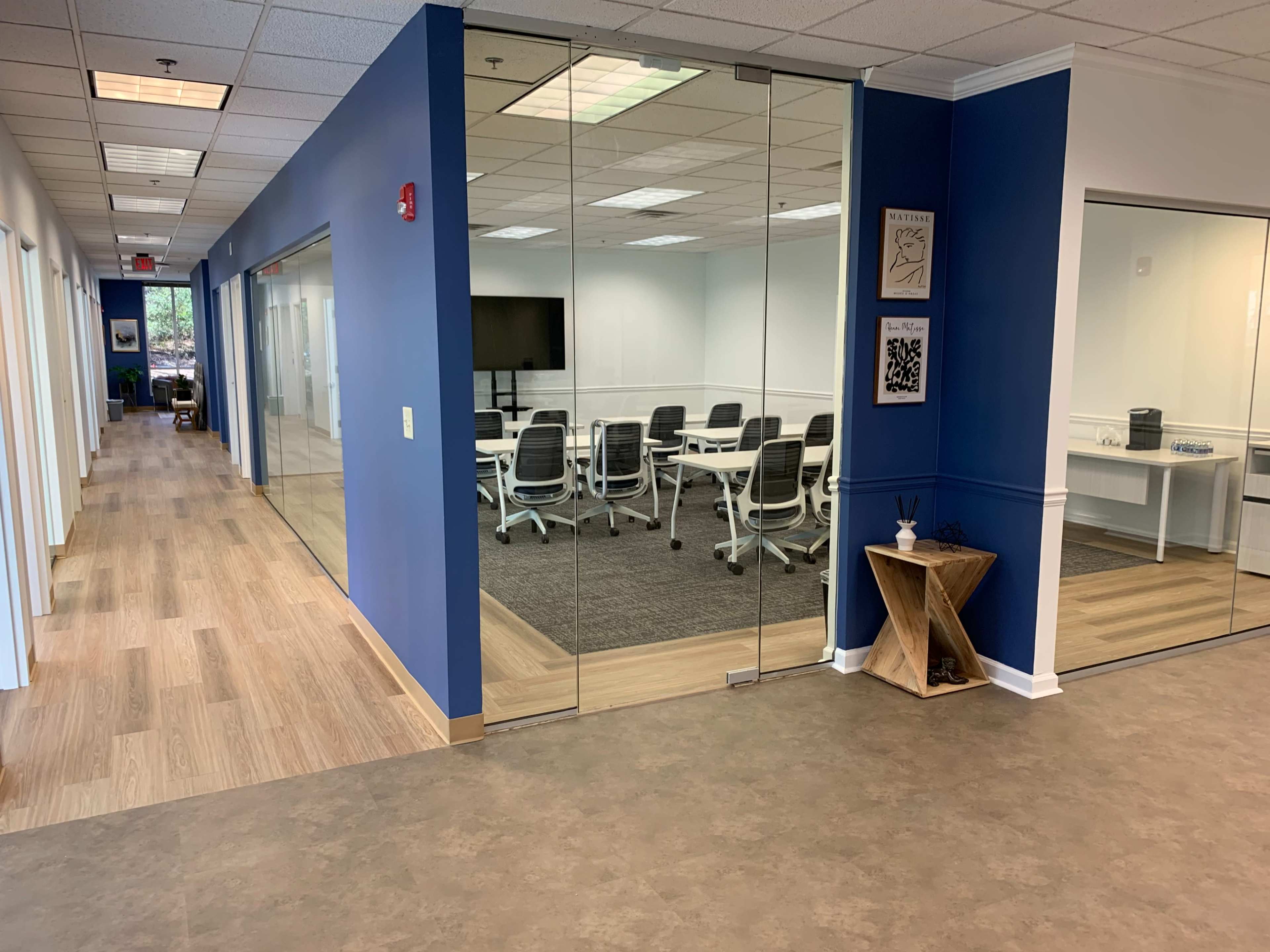 A modern office space with a blue accent wall, glass meeting room, and a hallway leading to other rooms.