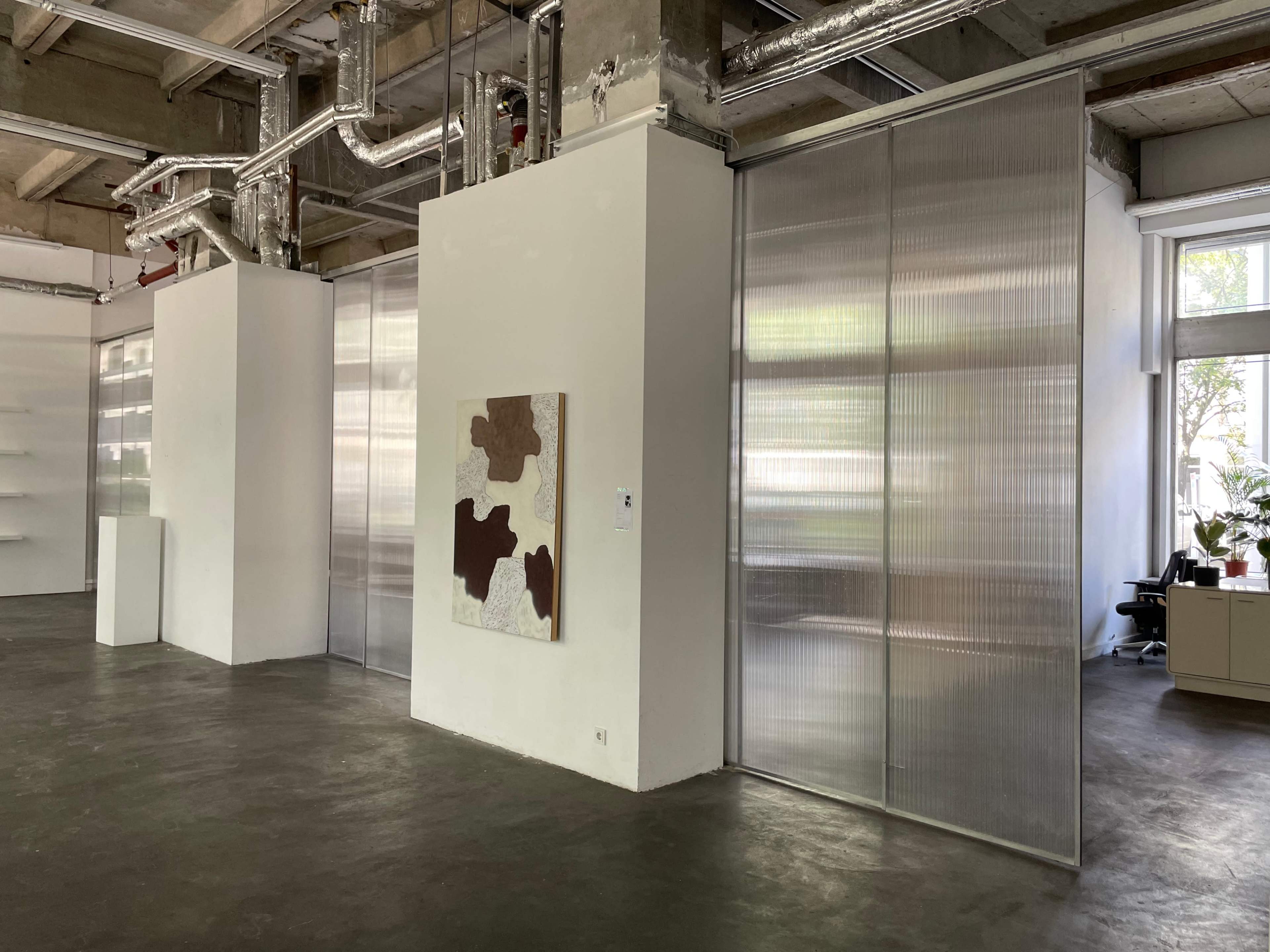 The image shows a spacious, modern interior with white walls, textured art on one wall, and sliding transparent doors dividing the space.