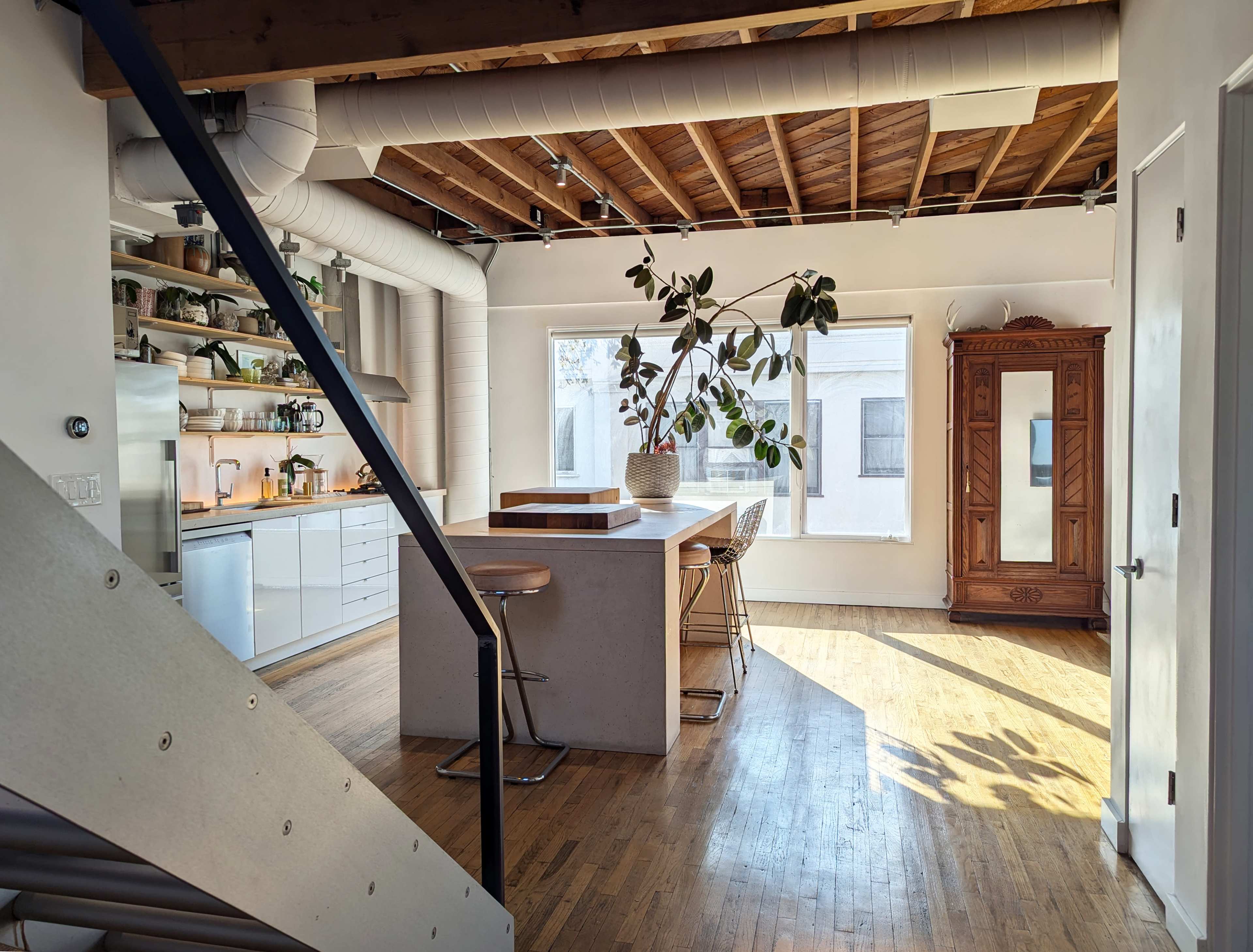 The image shows a modern kitchen with a wooden ceiling, a large island, and a dining area illuminated by natural light from large windows.